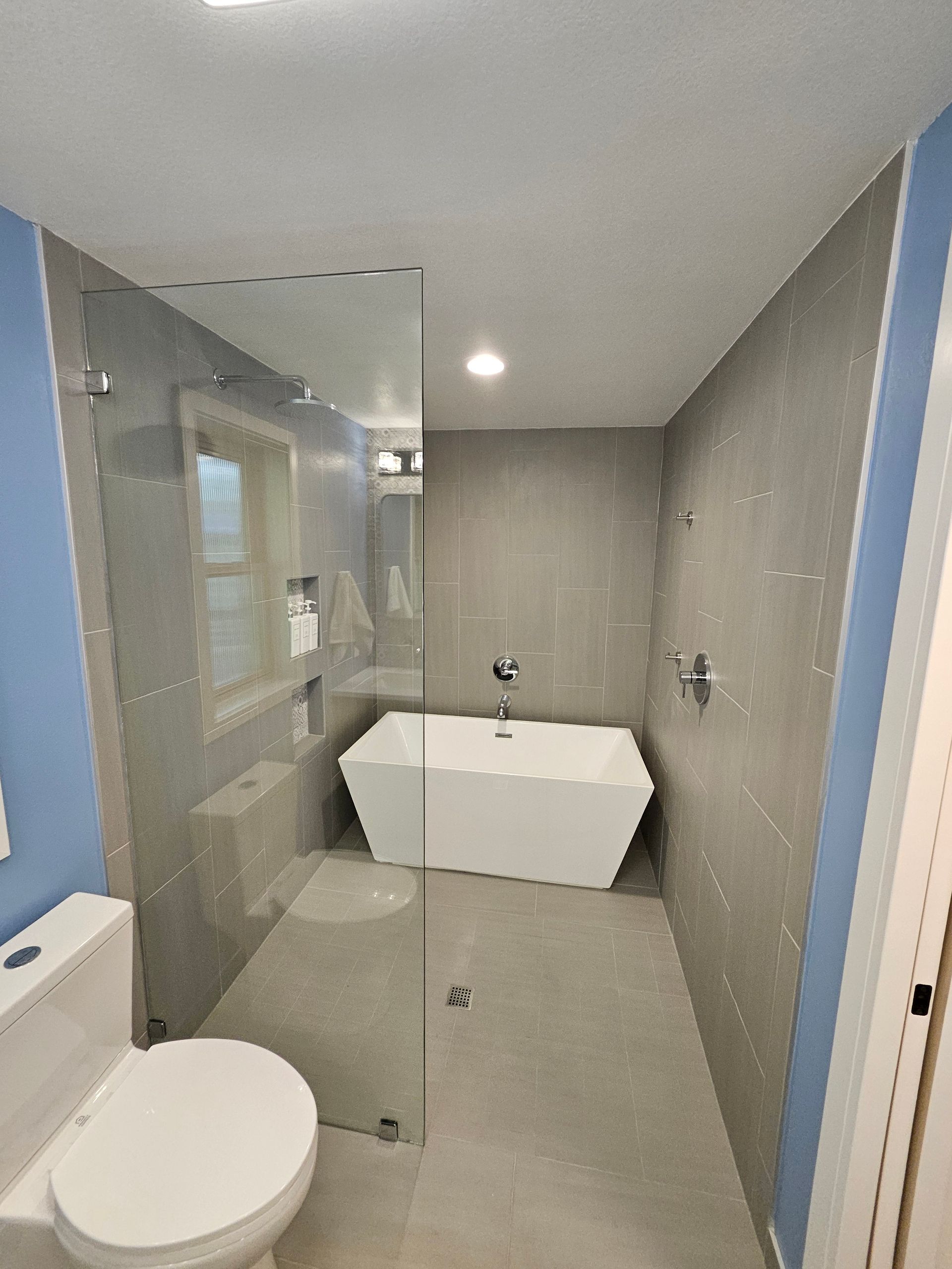 Modern bathroom with a white tub, toilet, and gray tiled walls.