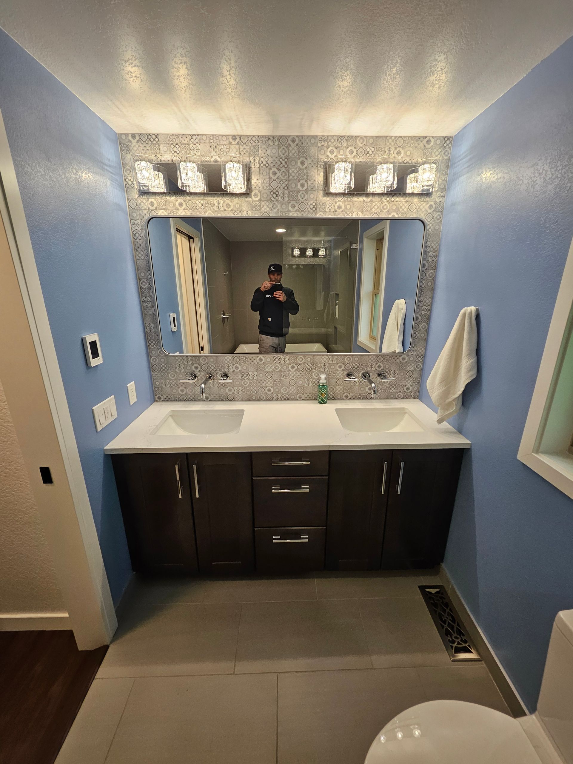 Bathroom with blue walls, dark brown vanity, double sinks, large mirror, and person reflected.