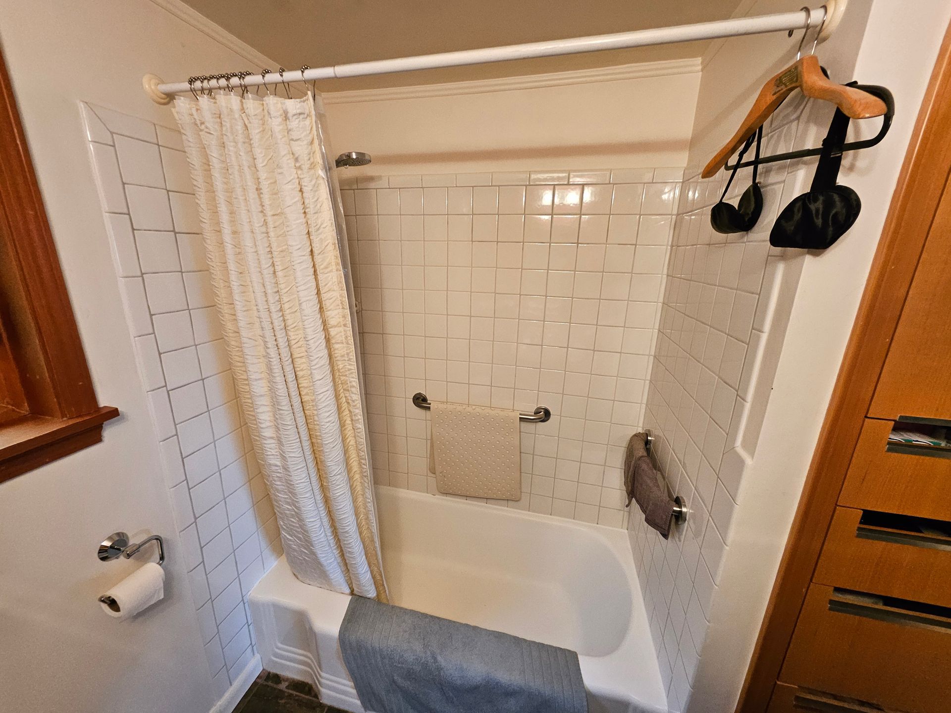 Bathroom with white tiled walls, a shower curtain, and a bathtub. A towel hangs over the edge.