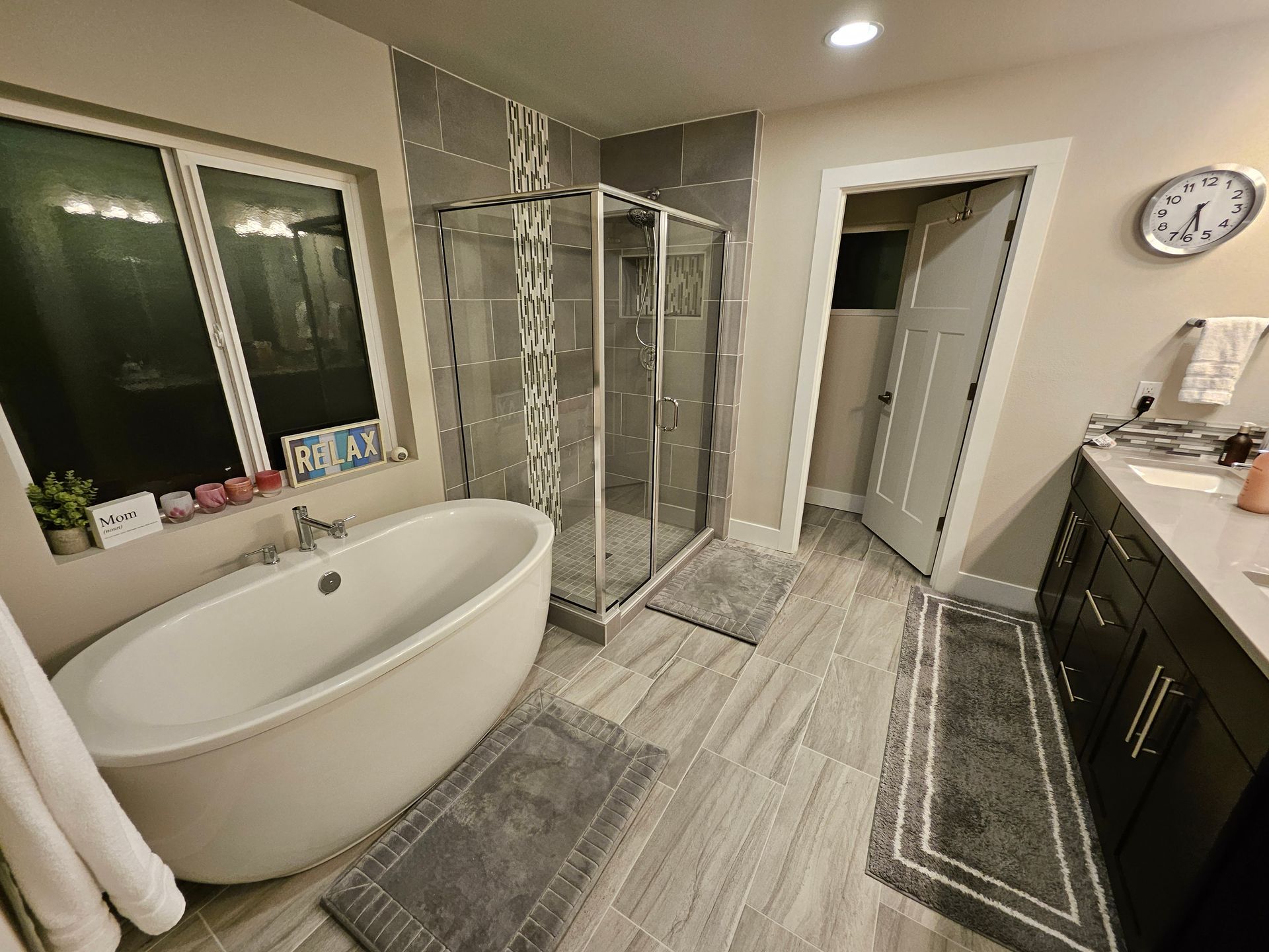Bathroom with a soaking tub, glass shower, and dark vanity. Gray and white color scheme.