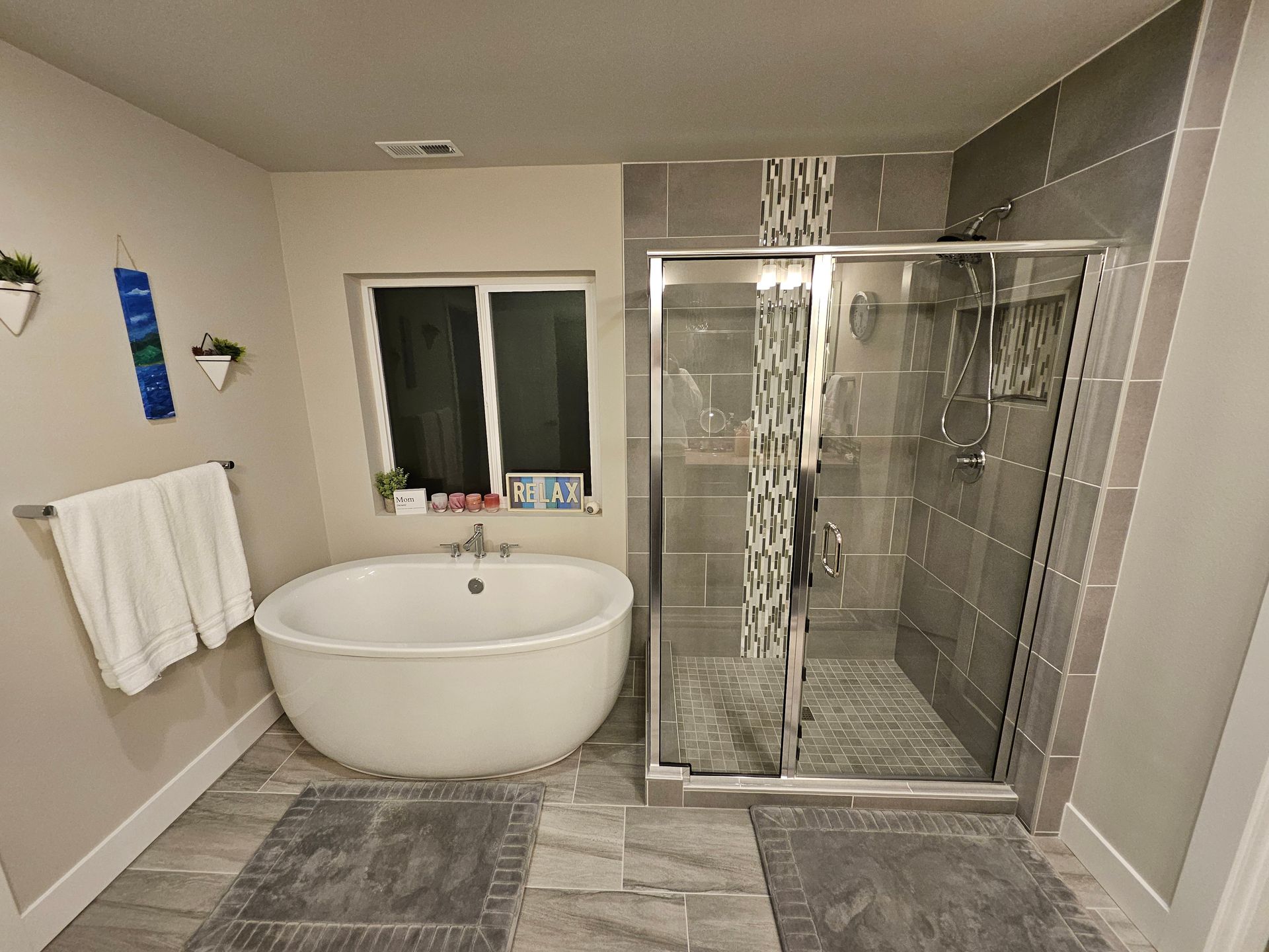 Modern bathroom with a round tub, glass shower, and gray tile. Towels hang near the tub.