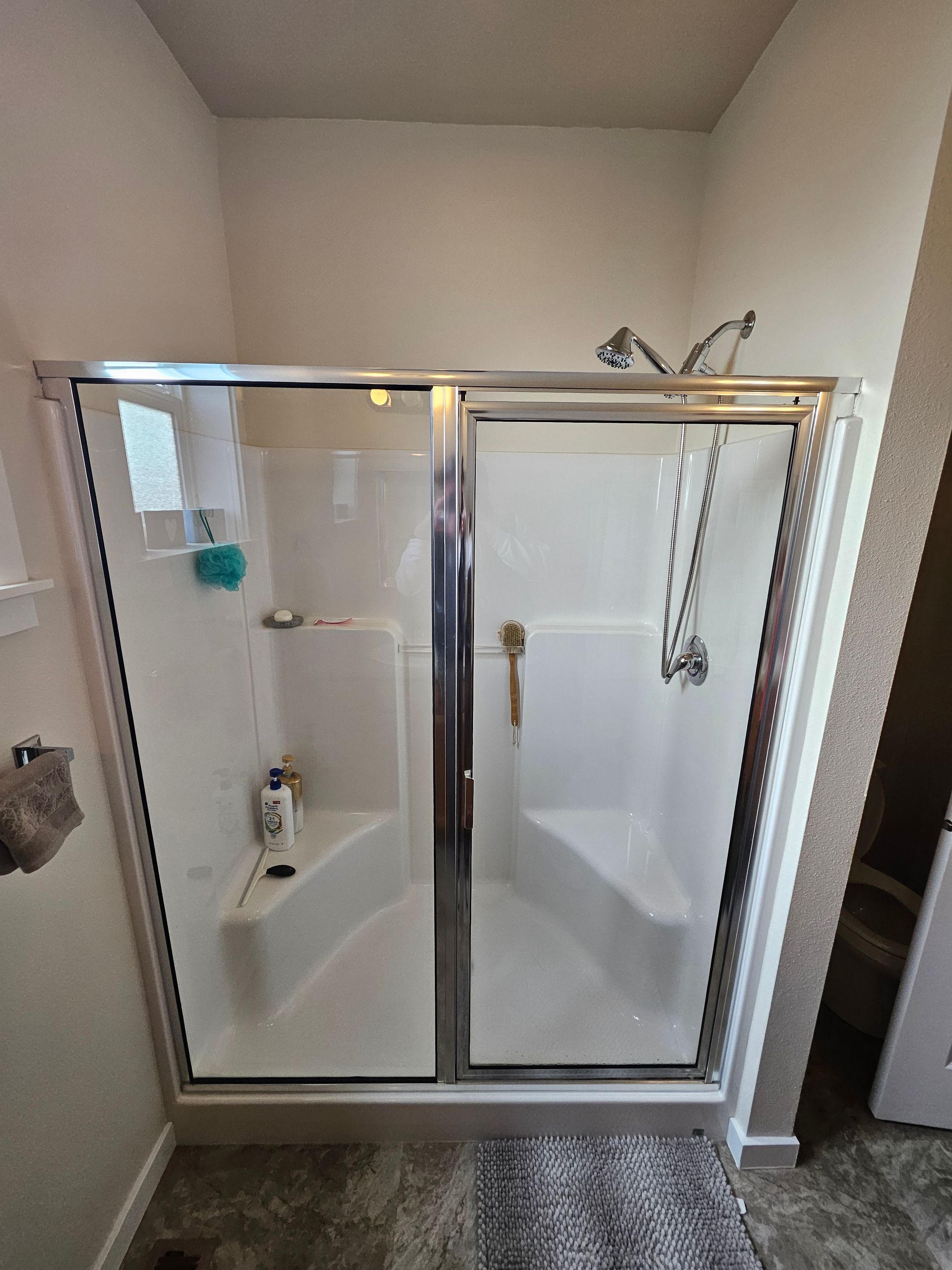A white shower stall with glass doors and a chrome frame in a bathroom.