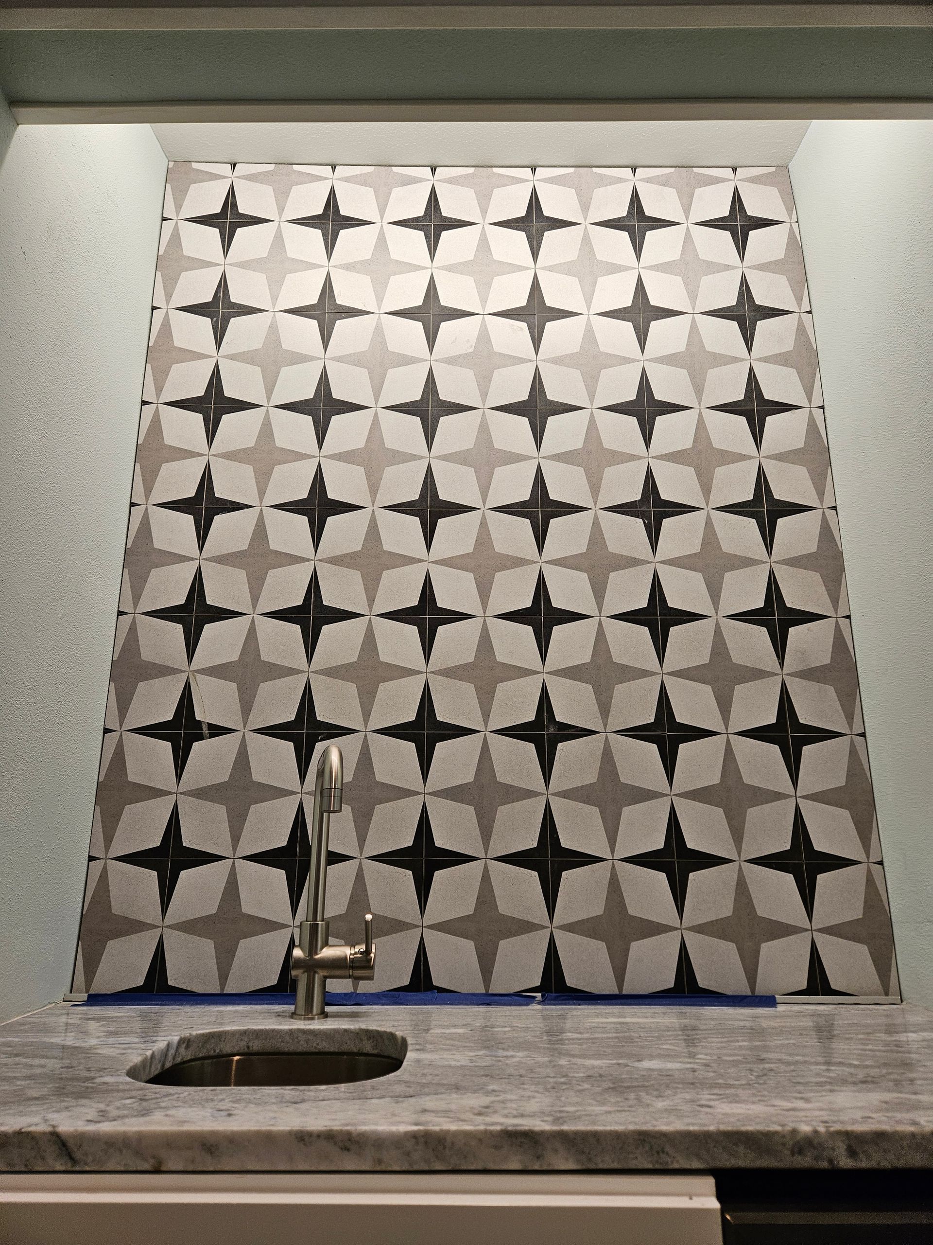 Sink with patterned star-shaped tile backsplash in shades of gray and black.