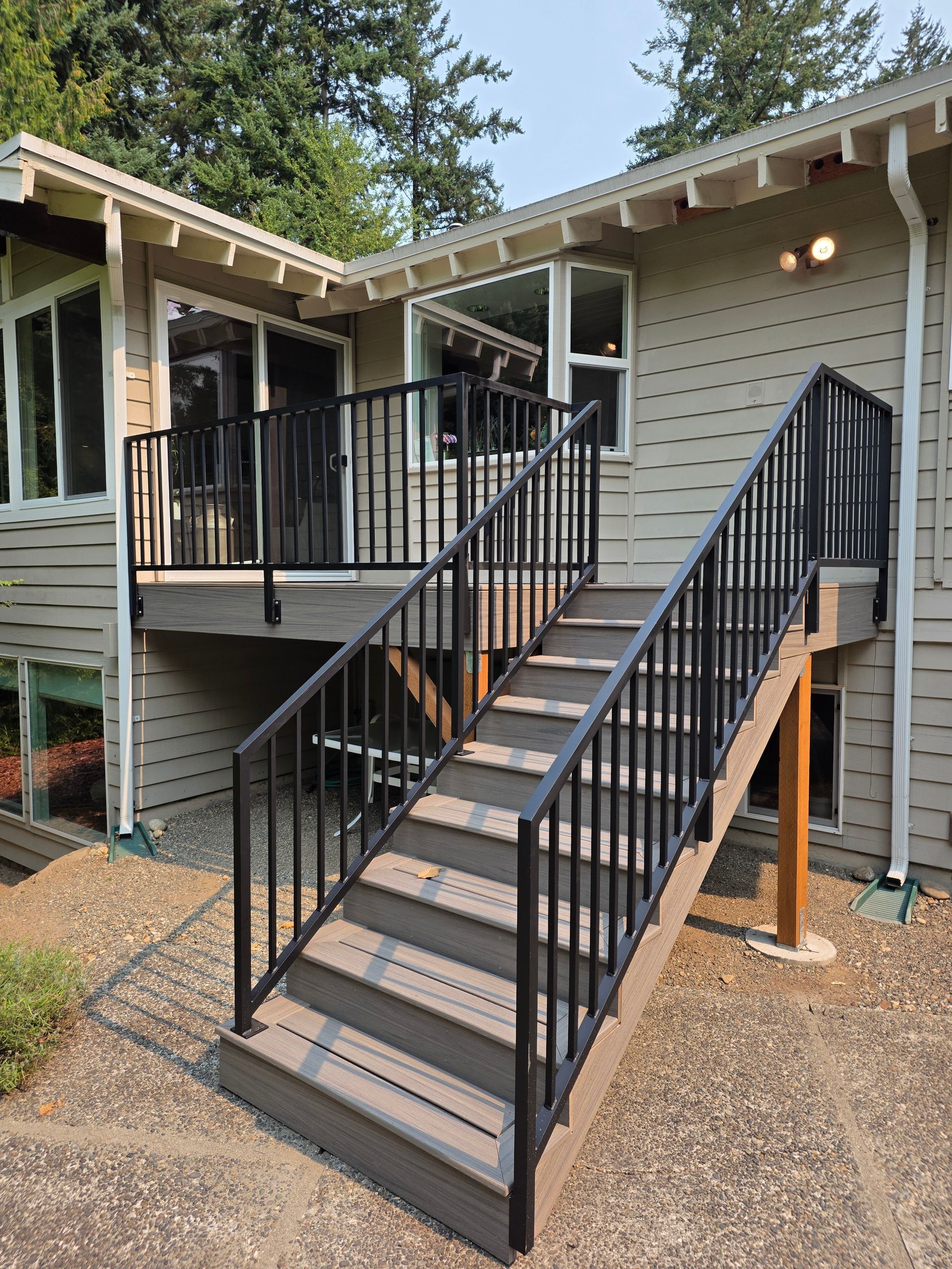 Exterior stairs with black metal railings leading to a deck attached to a house with beige siding.