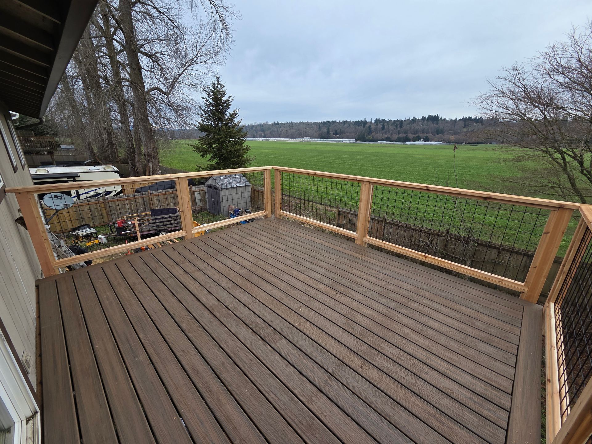 Wooden deck with metal railings overlooking a grassy field under an overcast sky.