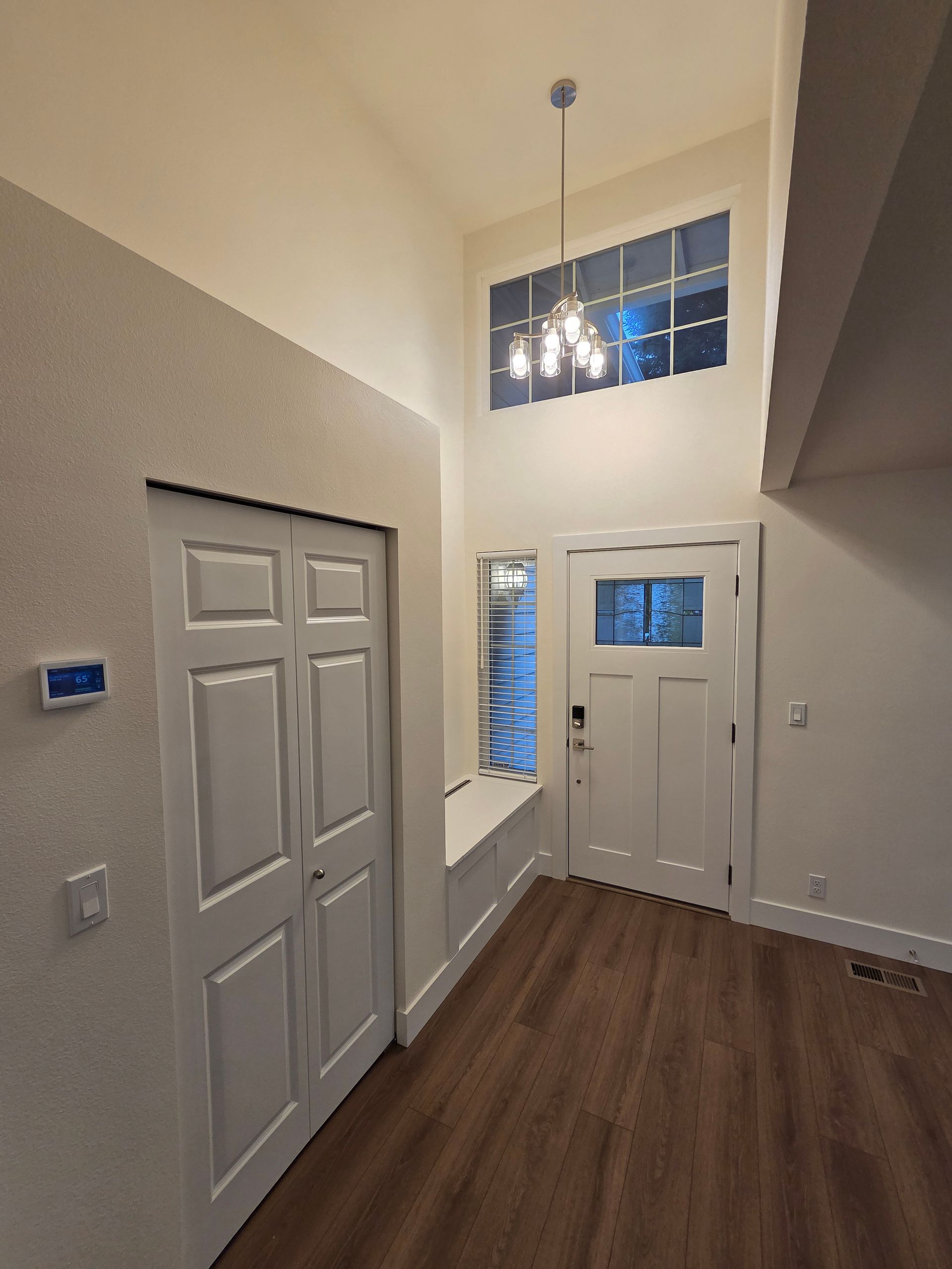 Entryway with white door, closet, window, and wood-look flooring. High ceiling with chandelier, tan and white walls.