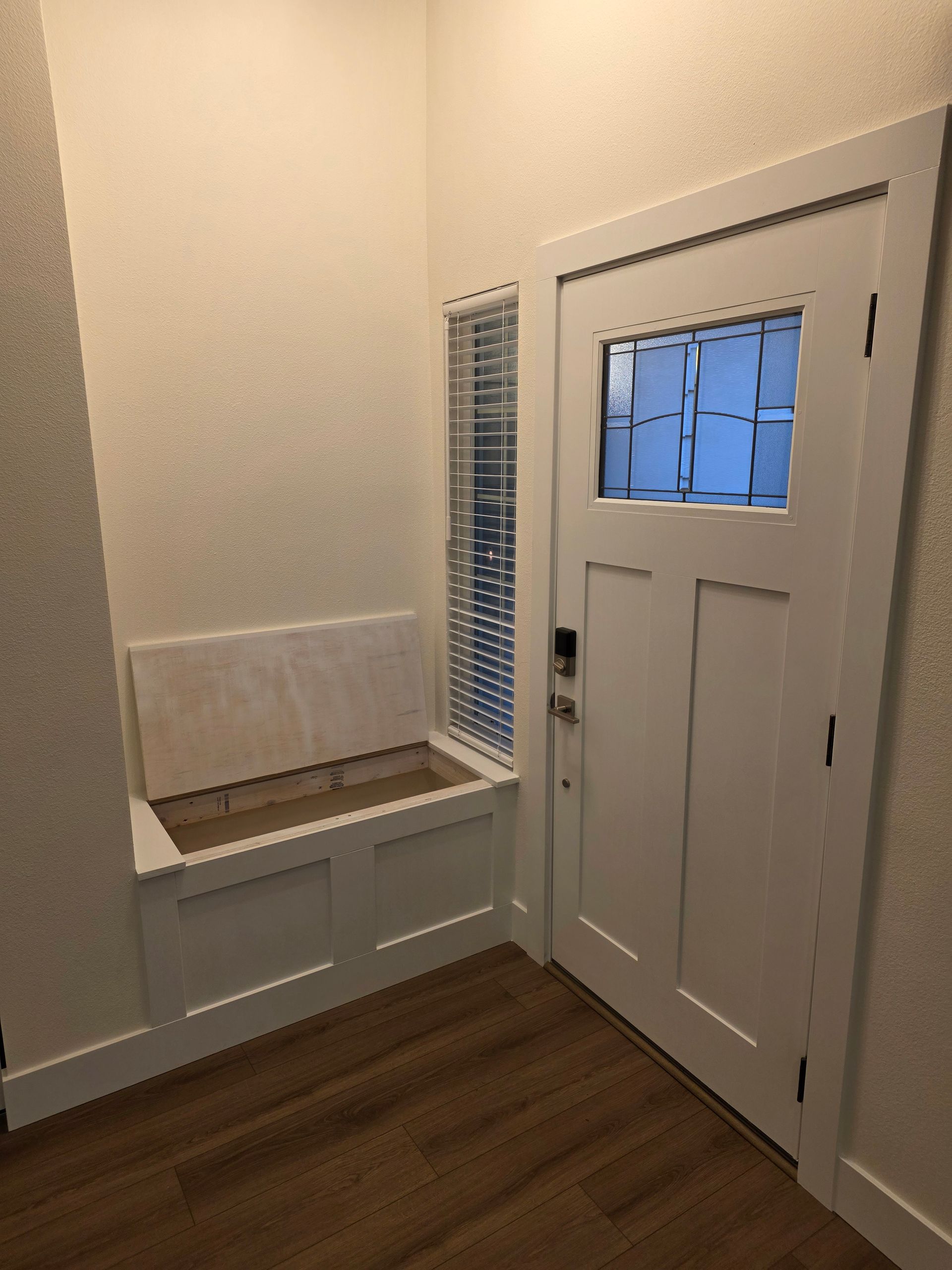 Entryway with white door, window, and built-in bench. Light-colored wood floor, white walls.