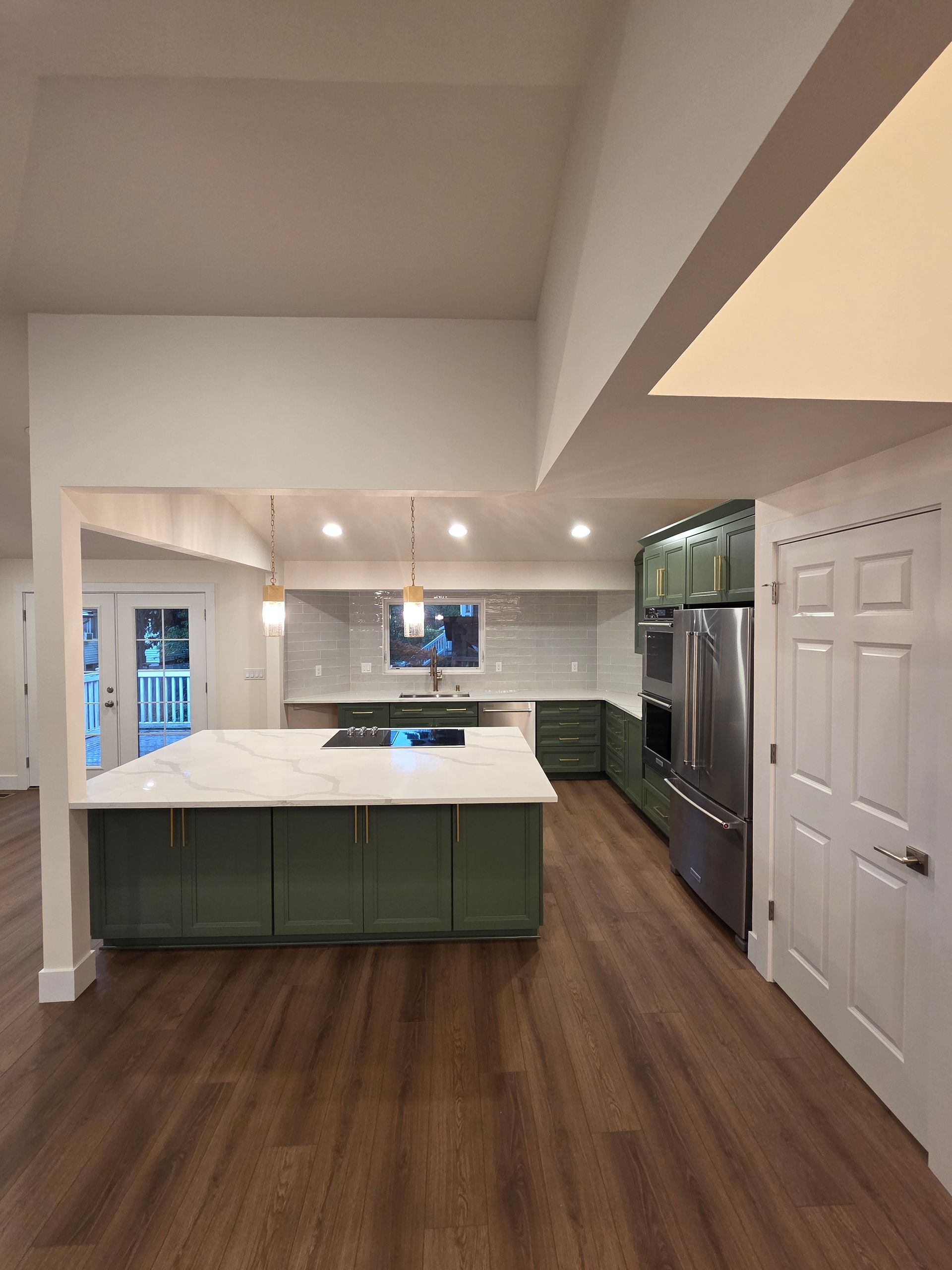 Modern kitchen with sage green cabinets, white island, and stainless steel appliances.