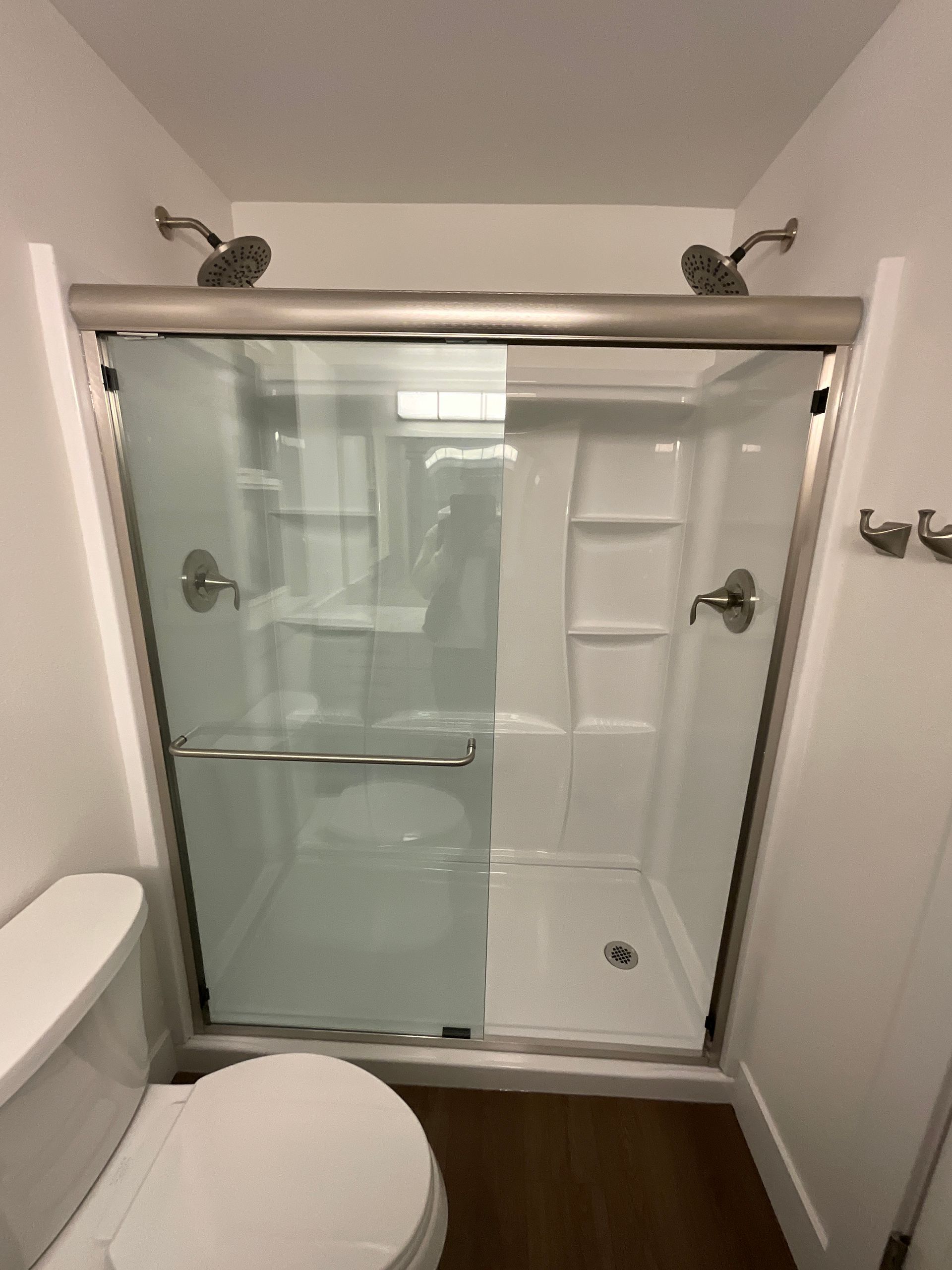 Shower stall with sliding glass doors, dual shower heads, and a toilet. White walls.