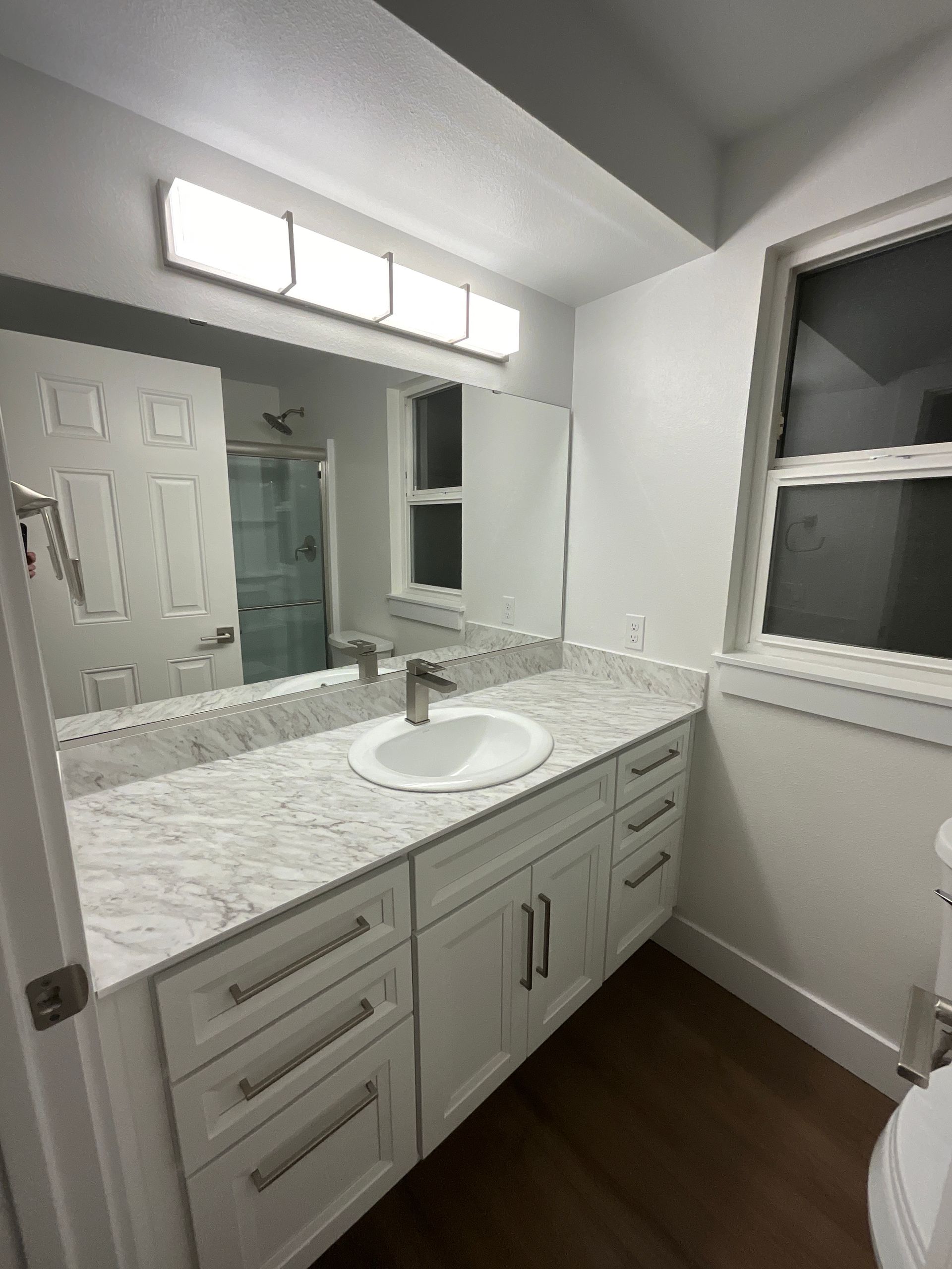 Bathroom with white vanity, marble countertop, large mirror, and window.