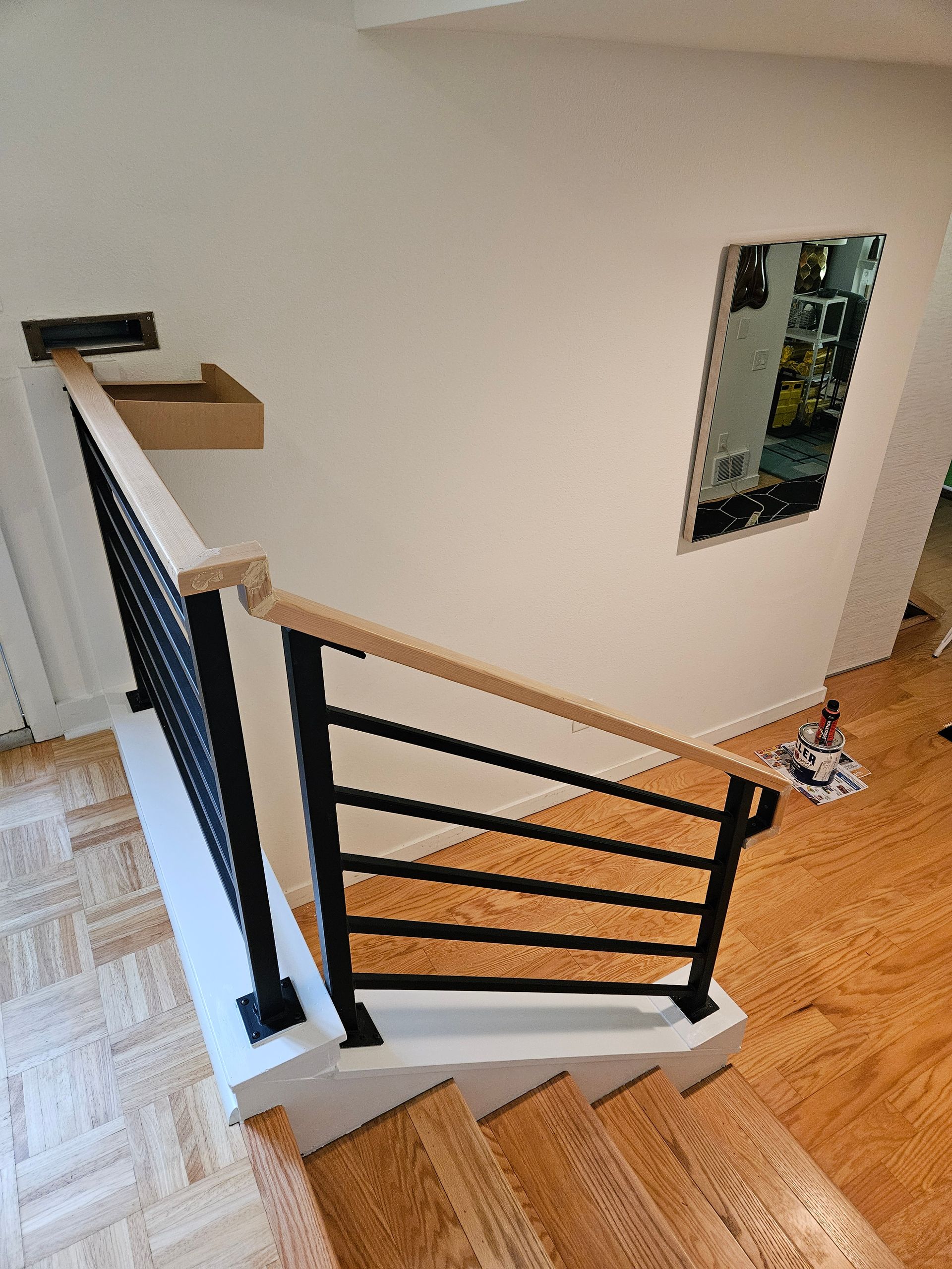 Modern staircase with black metal railing and wooden handrail, leading up to a white wall.