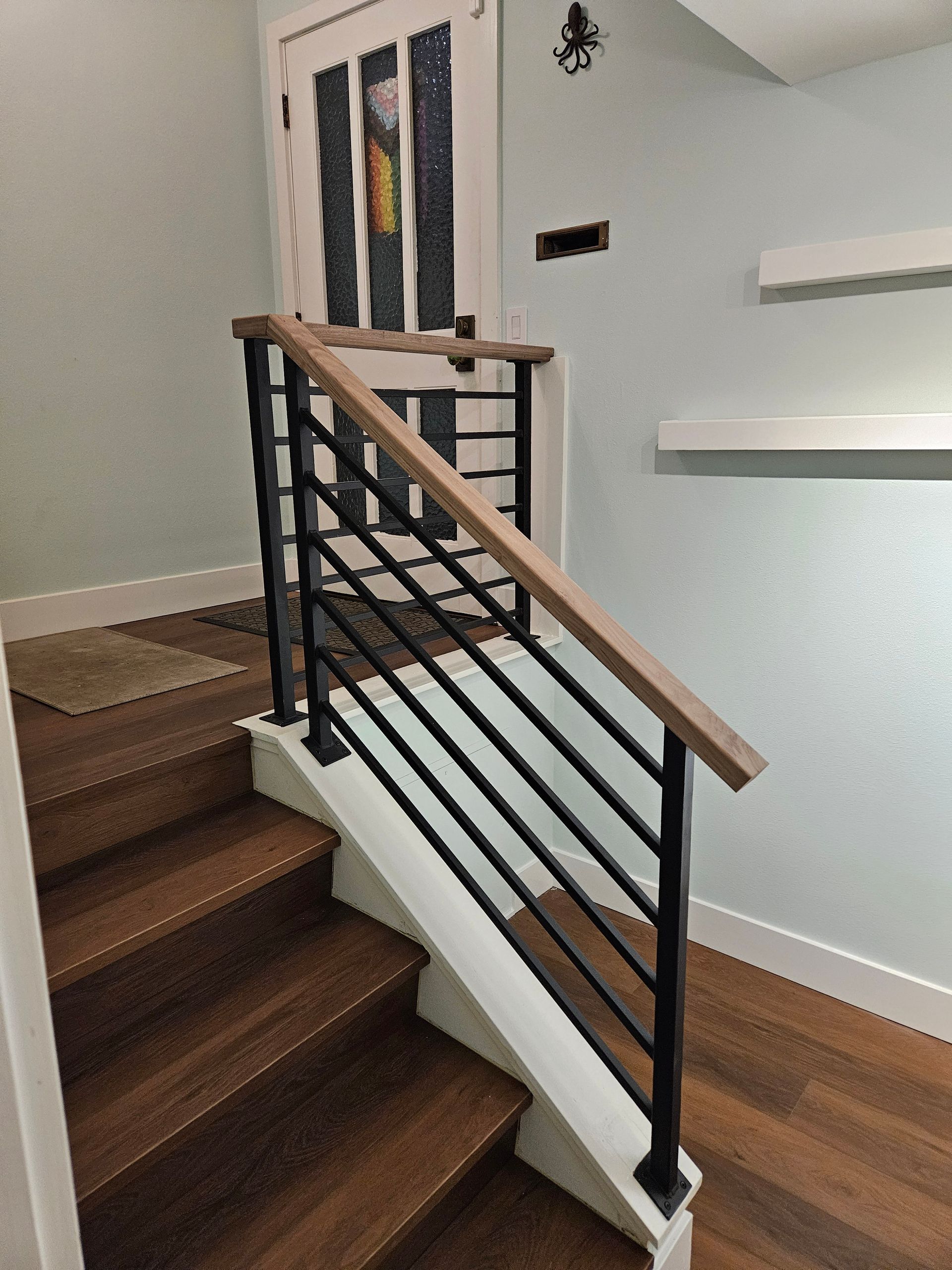 Staircase with wooden steps and railing, black horizontal bars and light wood handrail.
