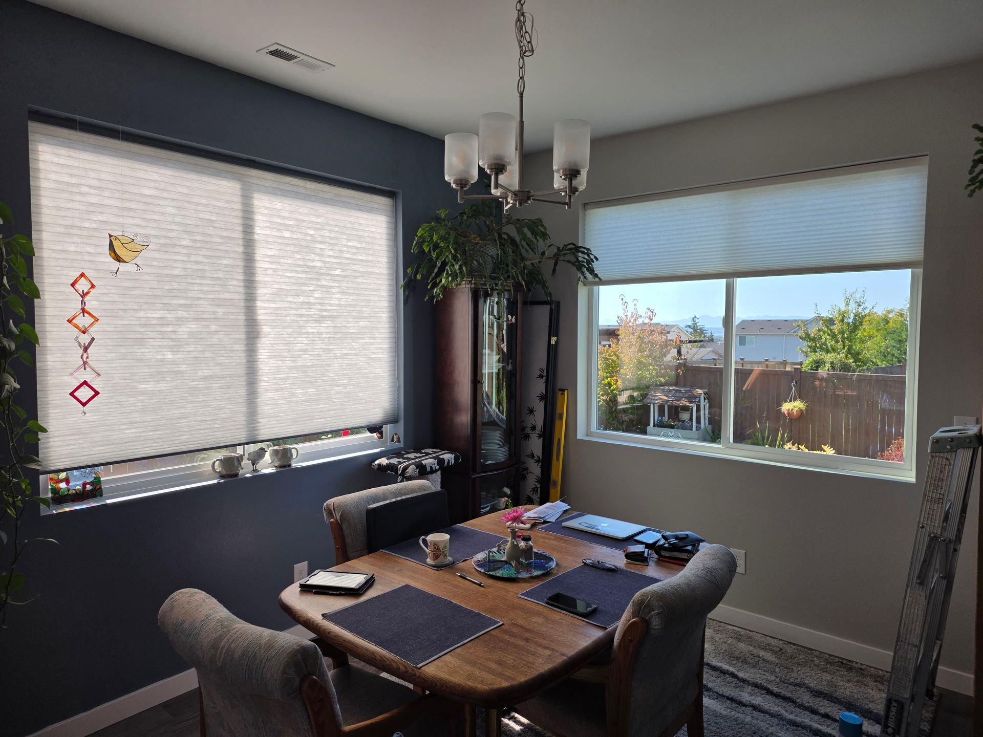 Dining room with table set for a meal, two windows with blinds, chandelier, and a dark accent wall.