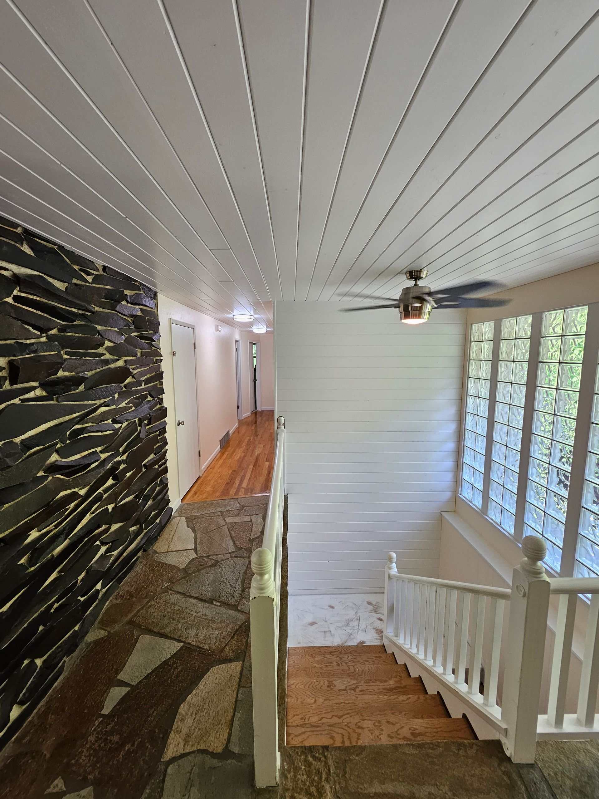 Hallway with stone wall, white ceiling, and staircase.