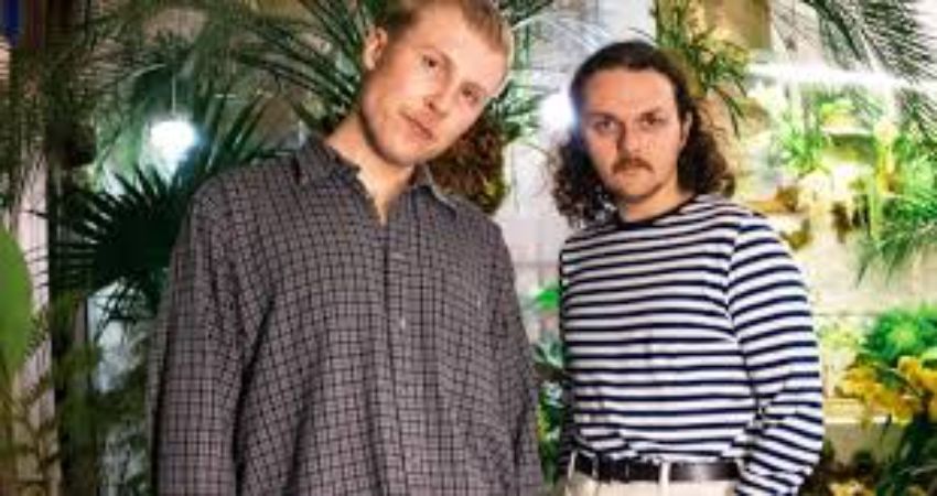 Two men are standing next to each other in front of a greenhouse.