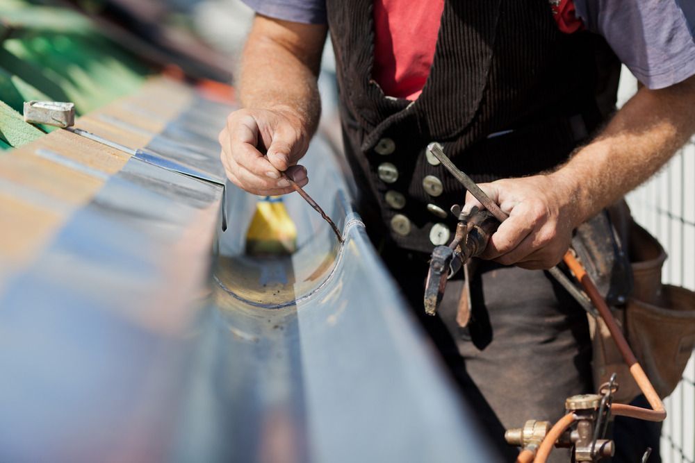 A Man Is Working On A Gutter With A Welding Machine — Dalrymple Sheet Metal In Garbutt, QLD
