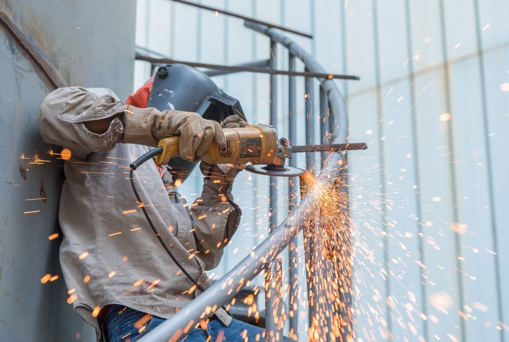 A Man Is Cutting A Metal Railing With A Grinder — Dalrymple Sheet Metal In Mount Isa, QLD