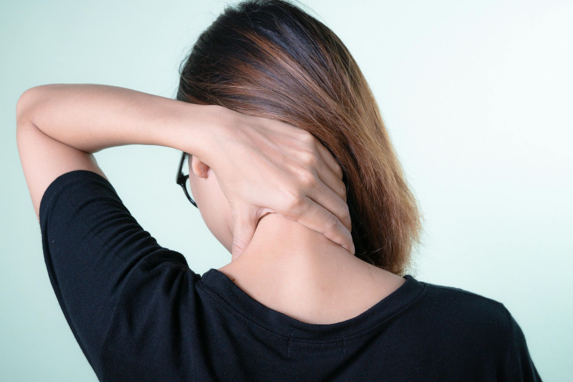 A woman is holding her neck in pain while wearing glasses.