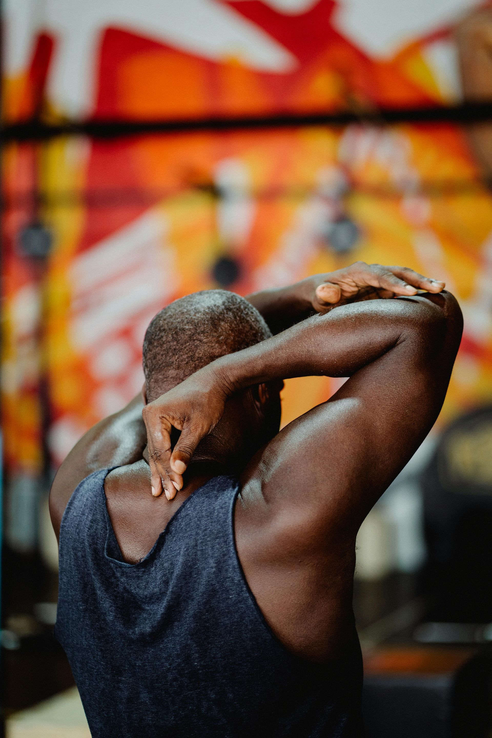 A man in a tank top is stretching his arms in a gym.