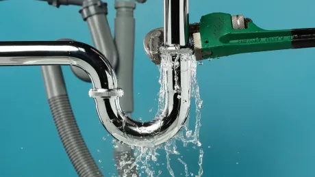 Leaking plumbing under a sink; water sprays out from a pipe held by a wrench, against a teal background.