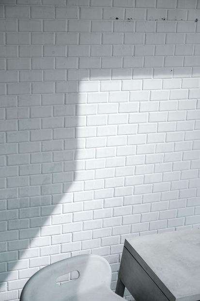 White brick wall, chair, and table with a diagonal shadow, natural light.
