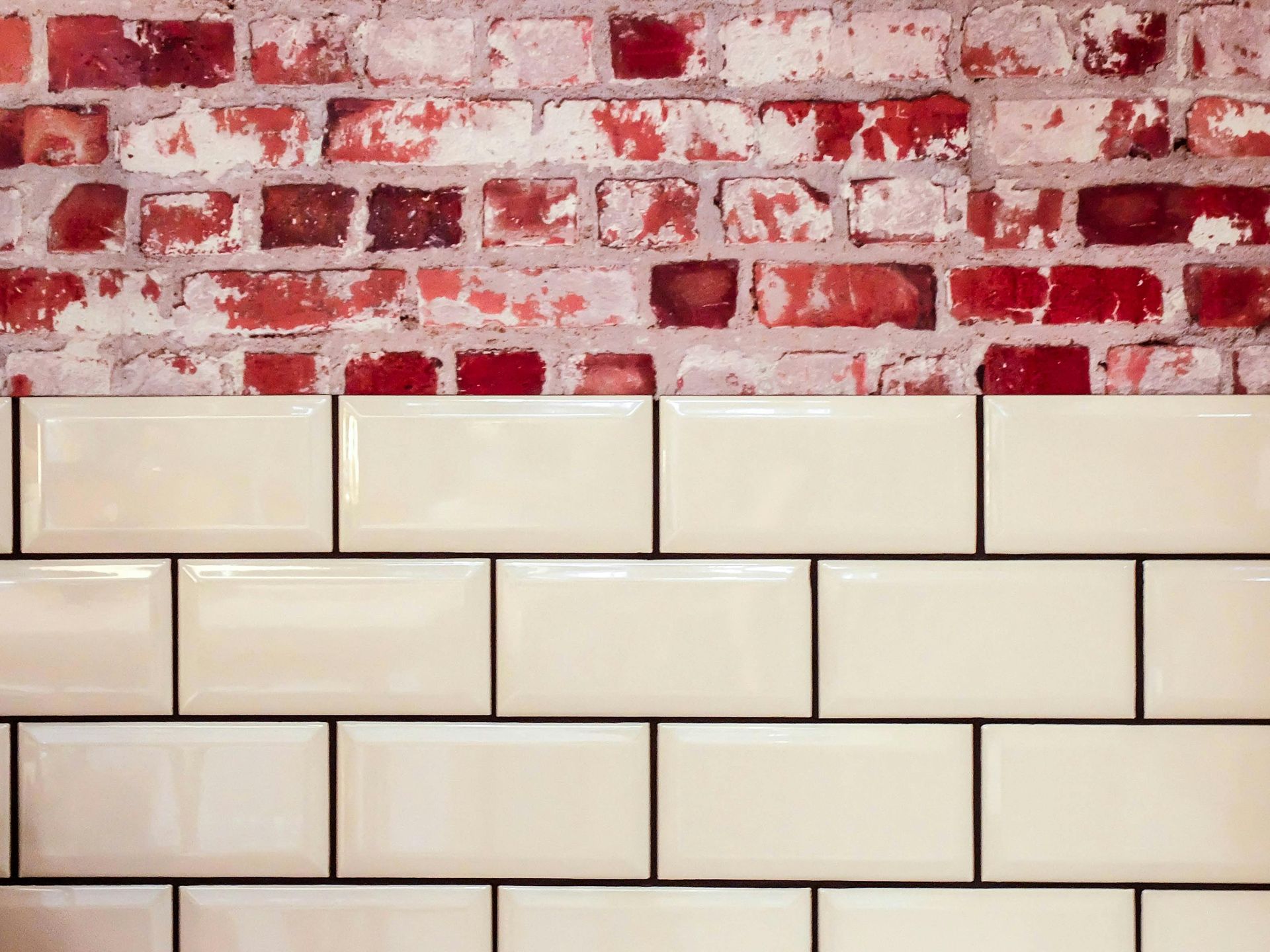 Brick wall above cream-colored rectangular tiles with dark grout lines.