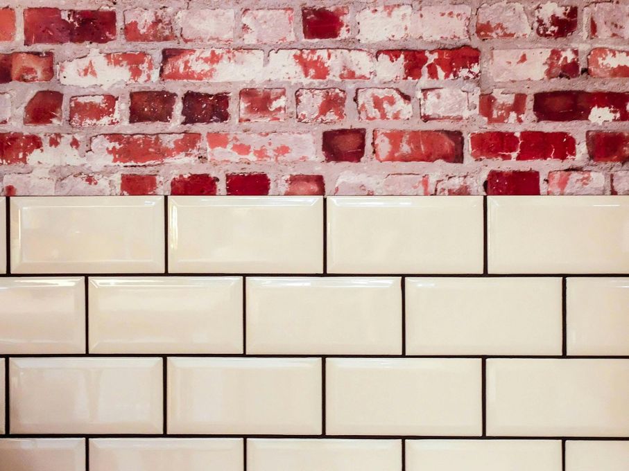 Brick wall above cream-colored rectangular tiles with dark grout lines.