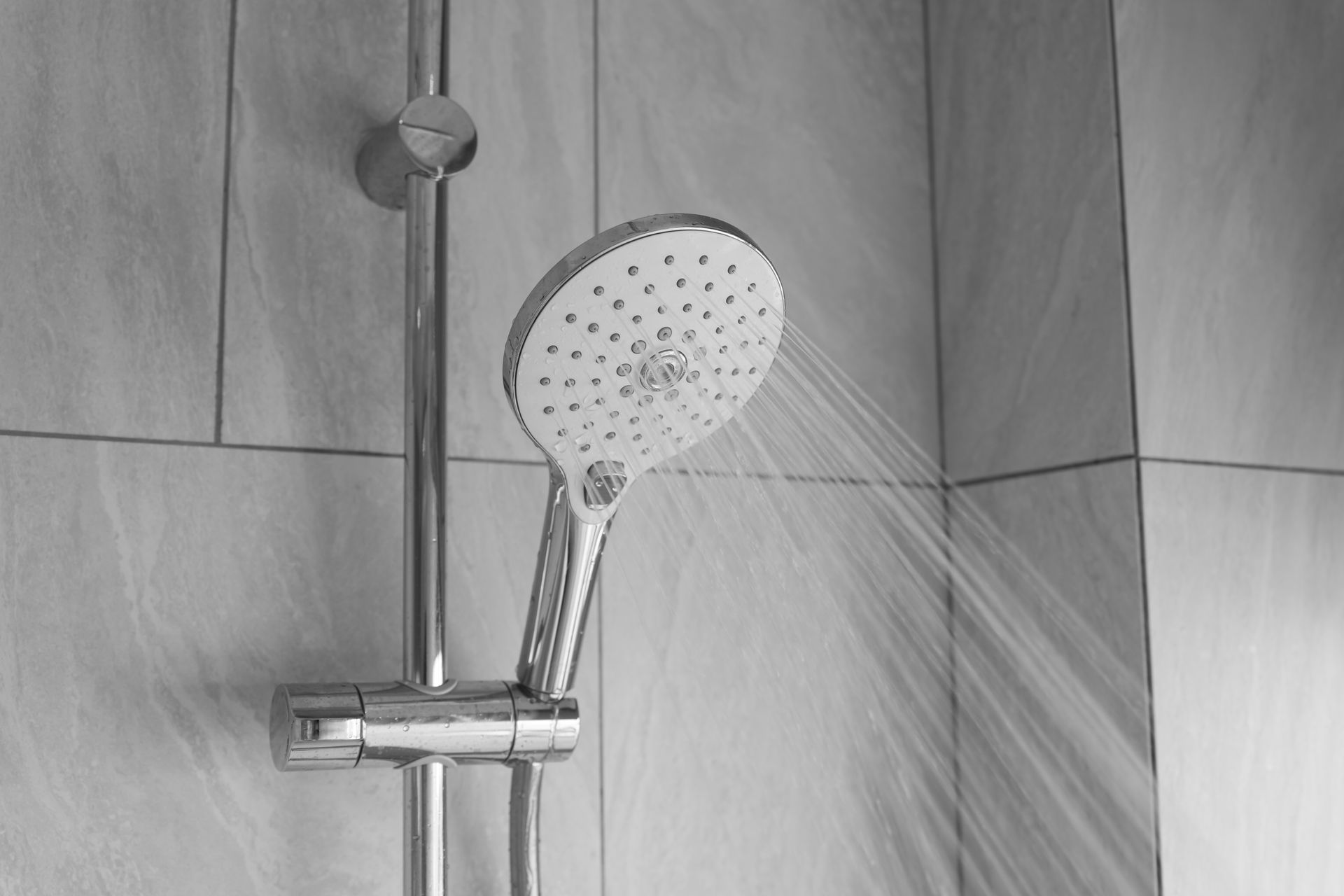 Showerhead with water spraying in a tiled shower.