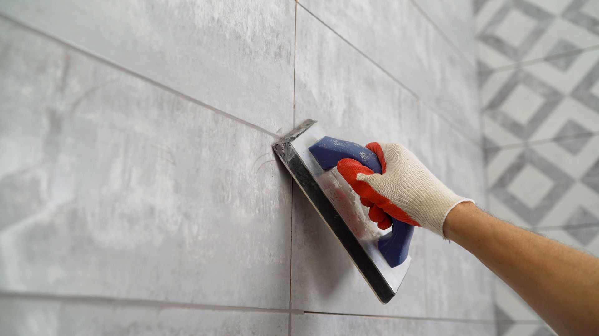 Person using a grout float to apply grout to wall tiles, close up view.