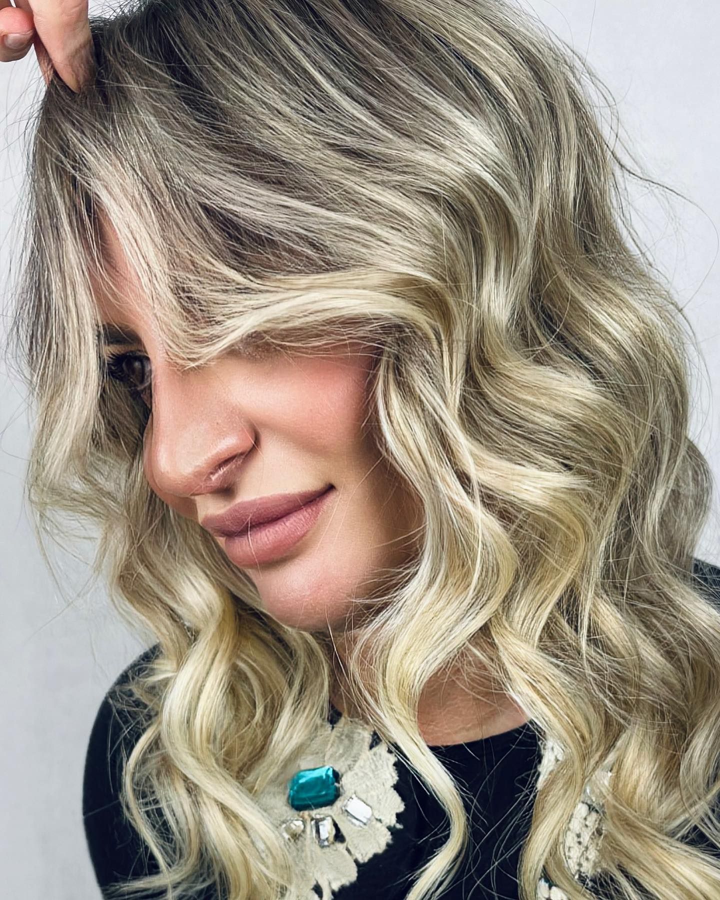 Una donna con lunghi capelli biondi e ondulati si copre il viso con i capelli.