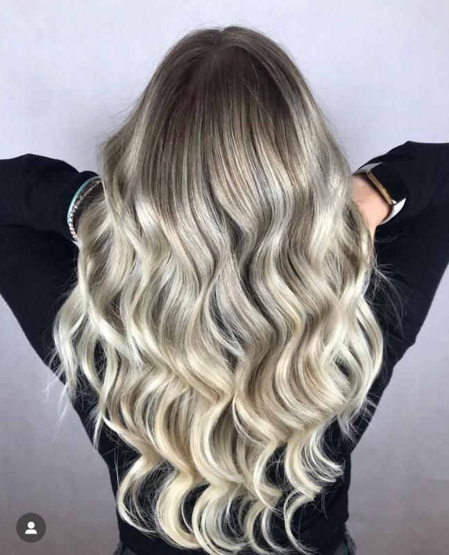 Una donna con lunghi capelli biondi e ondulati indossa una camicia nera.