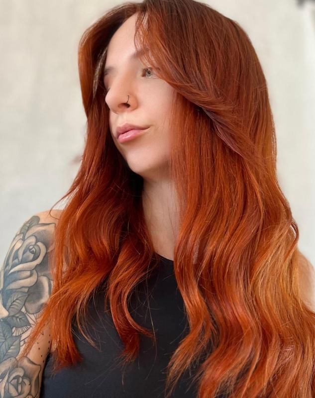 Una donna con lunghi capelli rossi e un tatuaggio sul braccio.