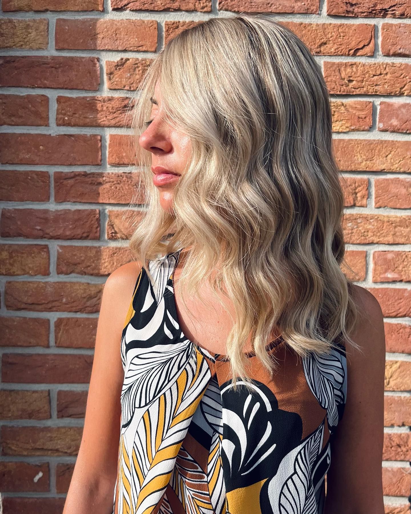 Una donna con i capelli biondi è in piedi davanti a un muro di mattoni.