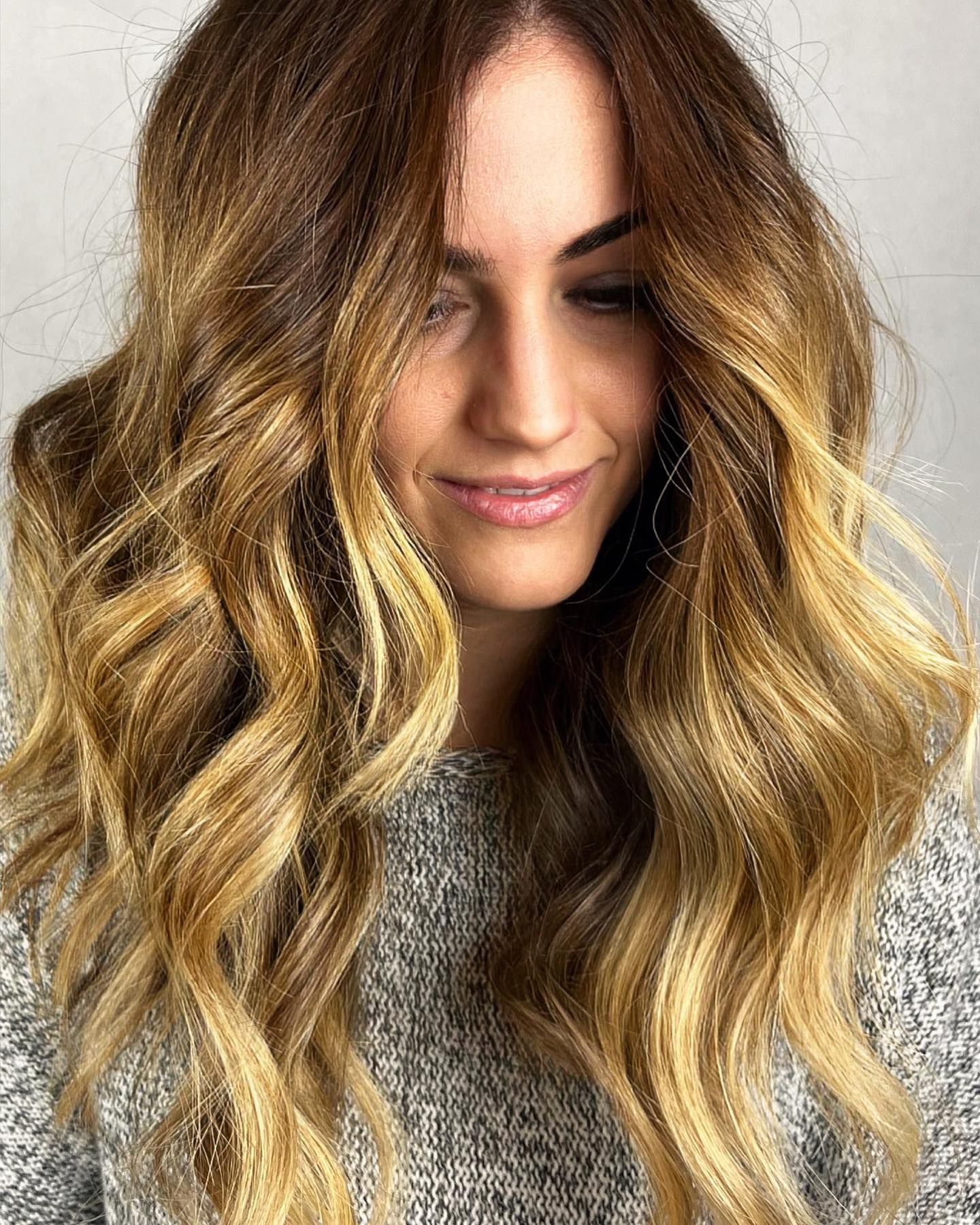 Una donna con lunghi capelli ondulati indossa un maglione grigio e sorride.