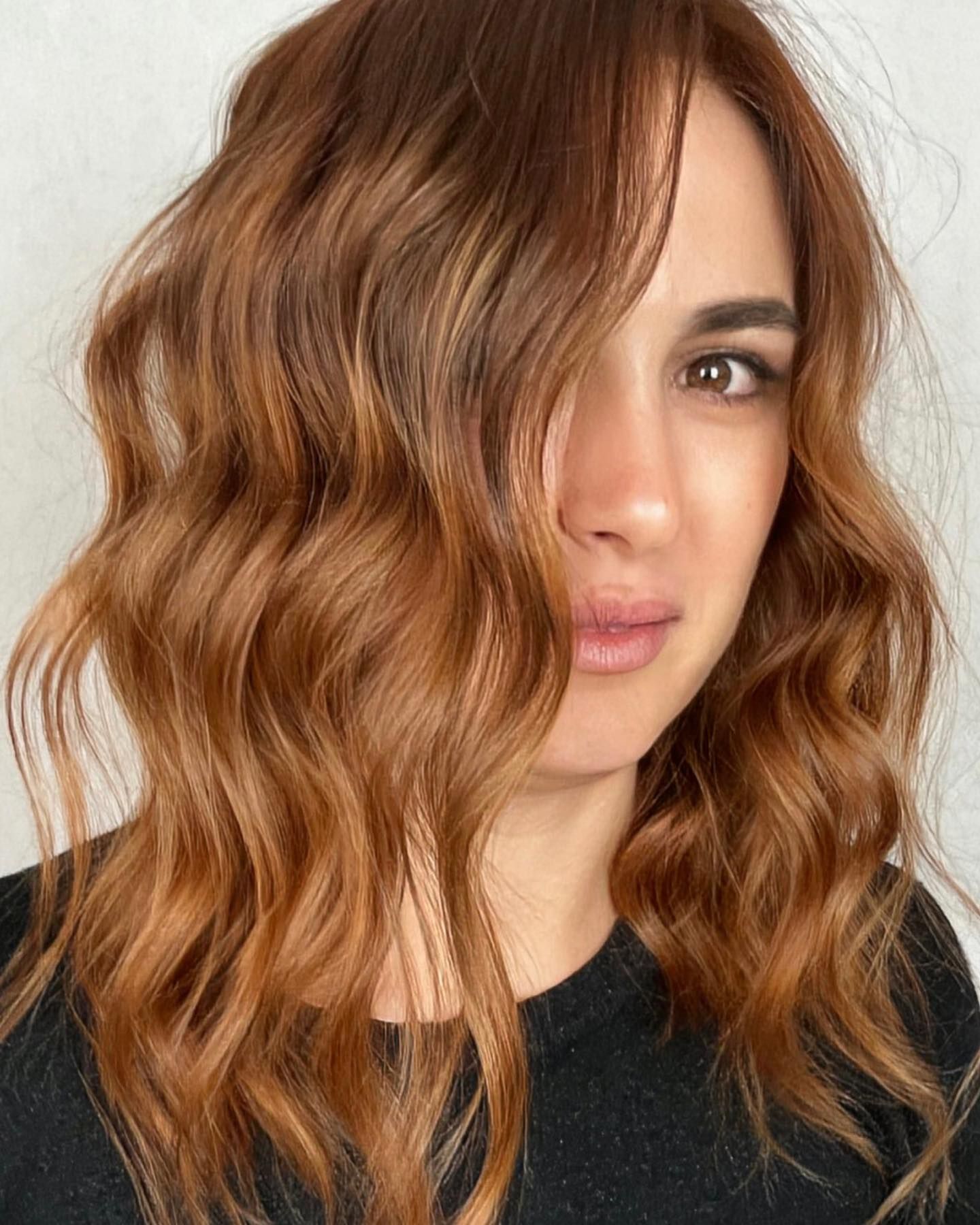 Una donna con lunghi capelli castani ondulati indossa una camicia nera.