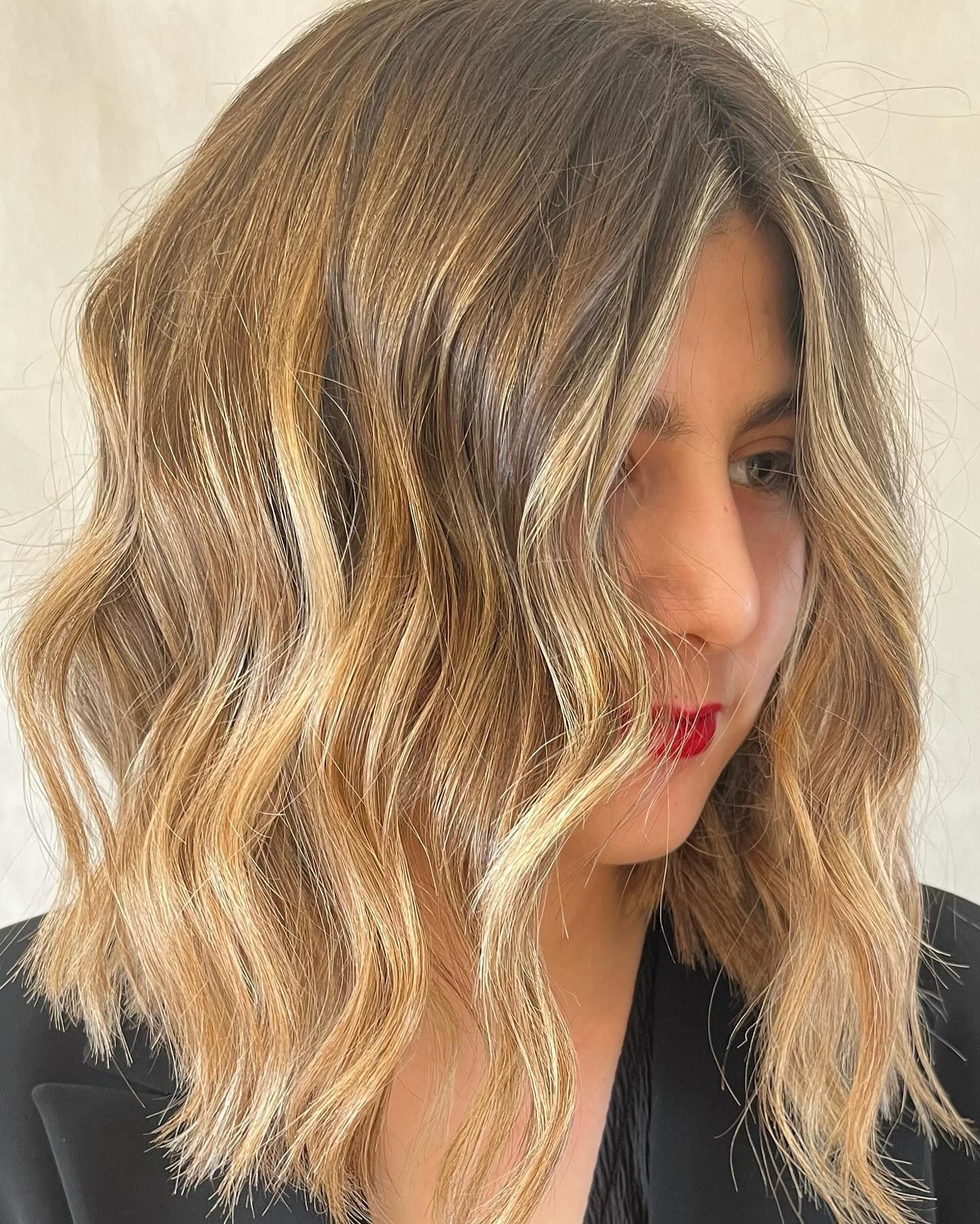 Una donna con lunghi capelli biondi e ondulati indossa una giacca nera.