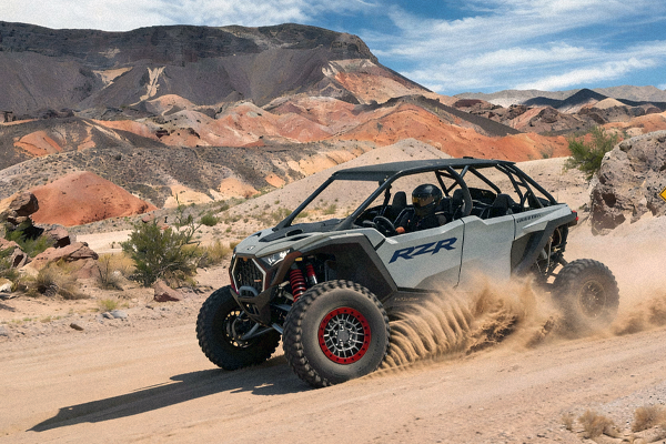 Gray Polaris RZR off-road vehicle driving on a dirt road, kicking up dust. Desert landscape backdrop.