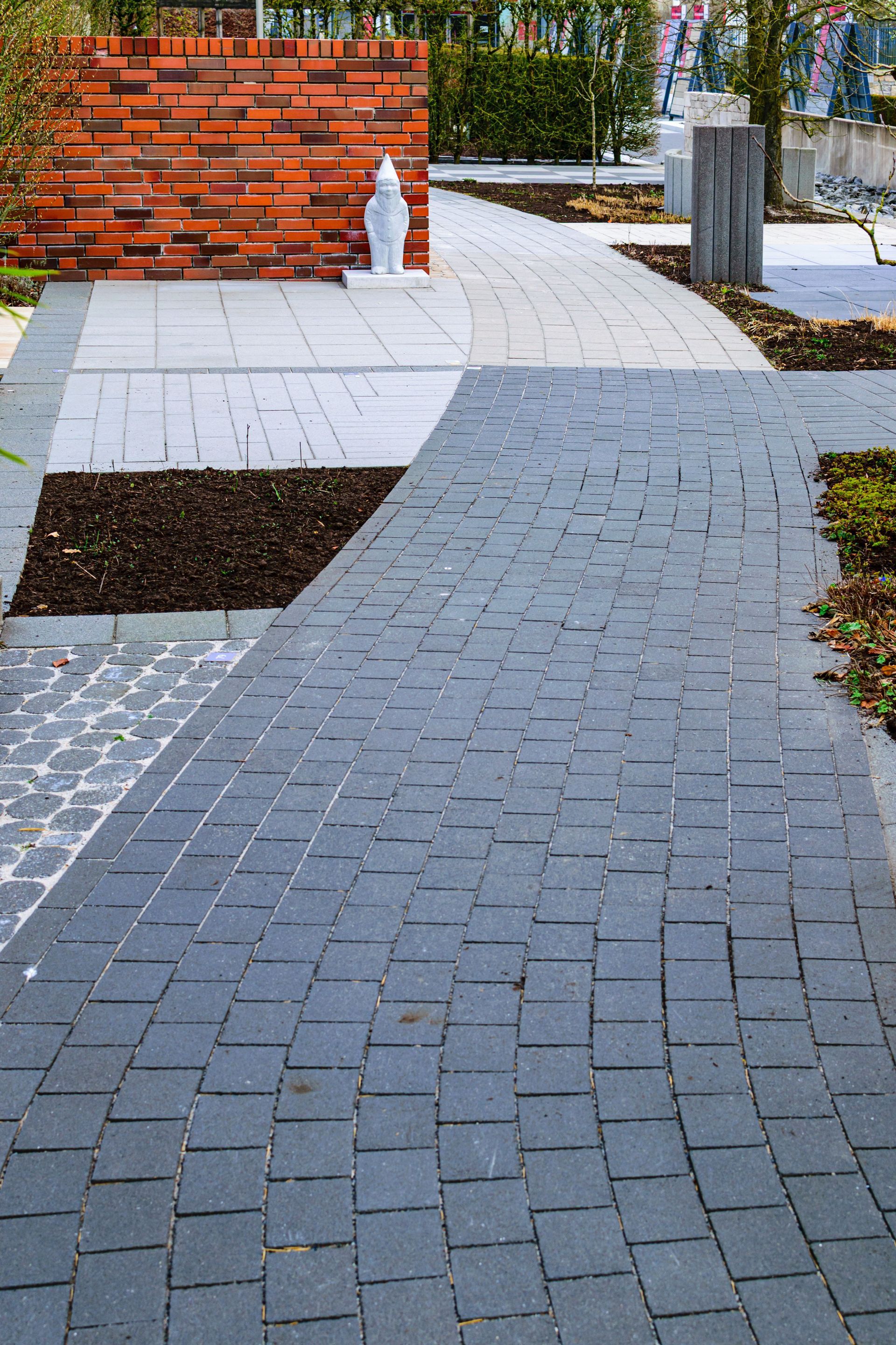 Brick-paved walkway with white benches, a red brick wall, and small trees in a park.