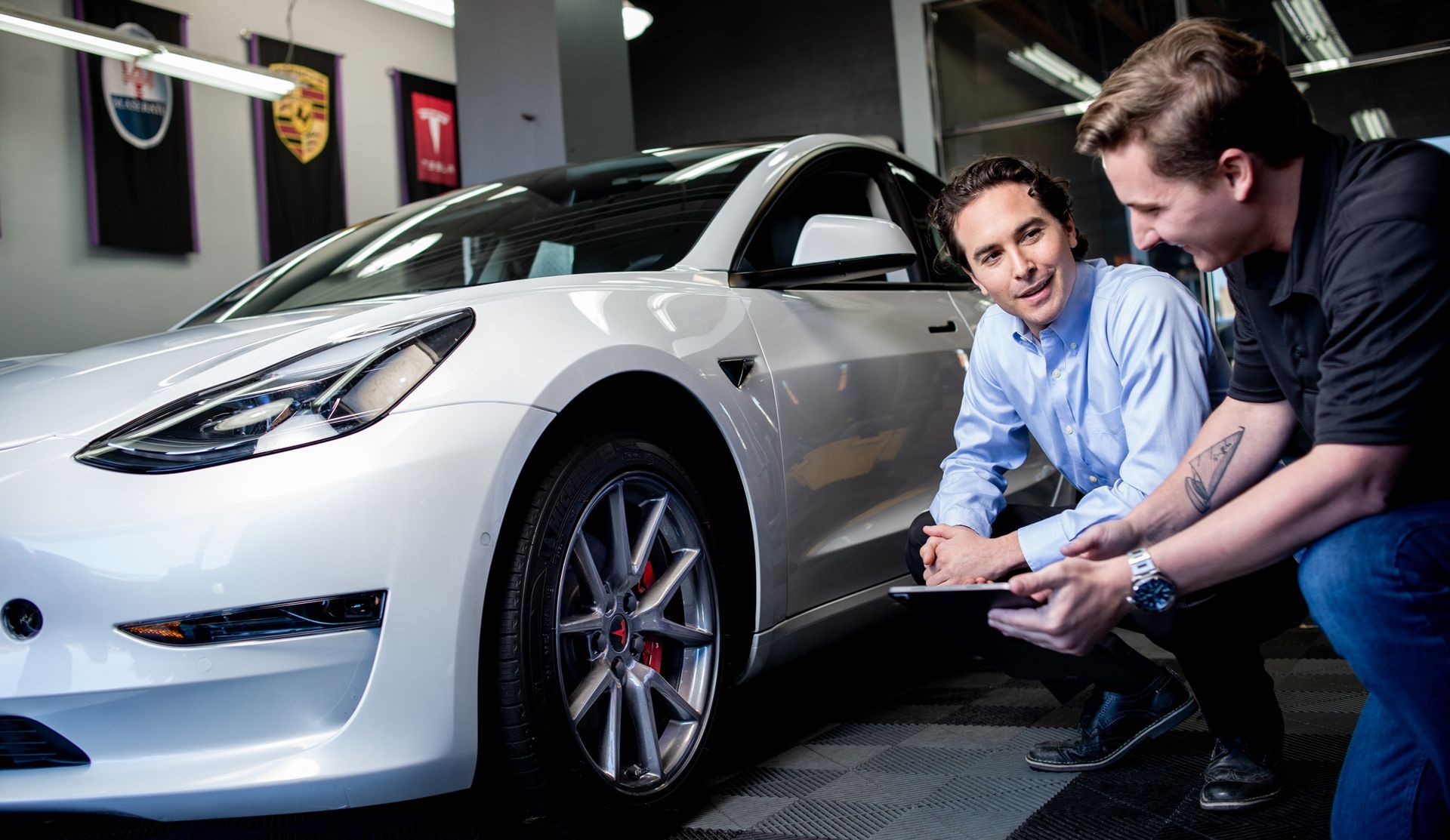 Two men are looking at a tesla model 3 in a garage.