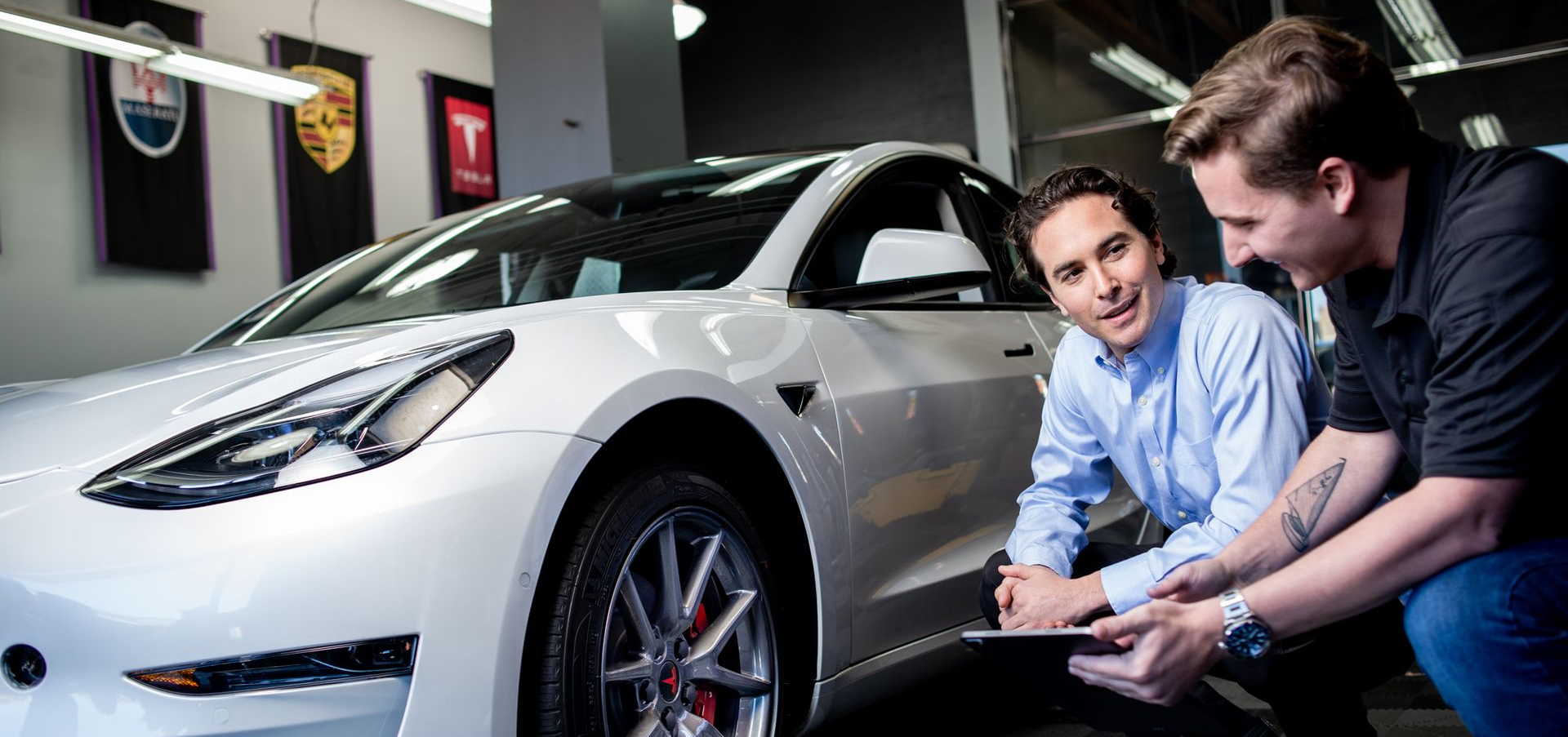 Two men looking at a document beside a white Tesla in a dealership.