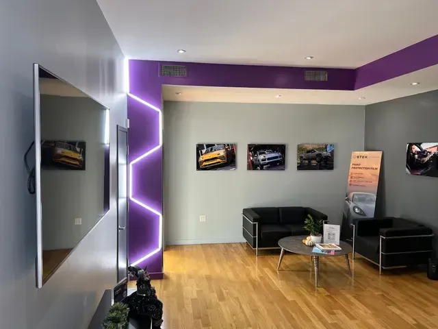 A waiting room with black furniture, art of cars, purple accent lighting, and wood floors.