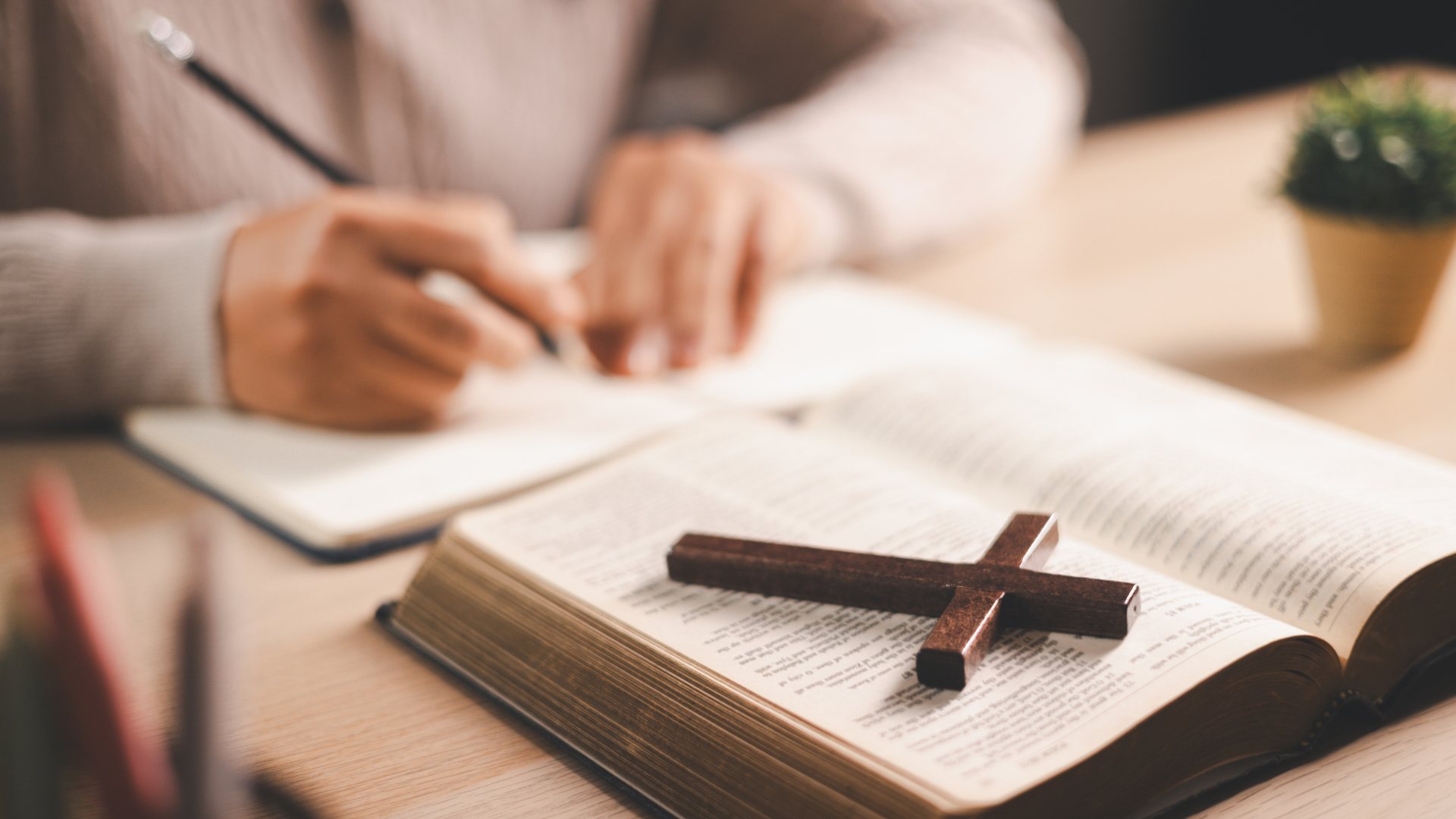 Person writing in a notebook beside an open book and pen on a desk