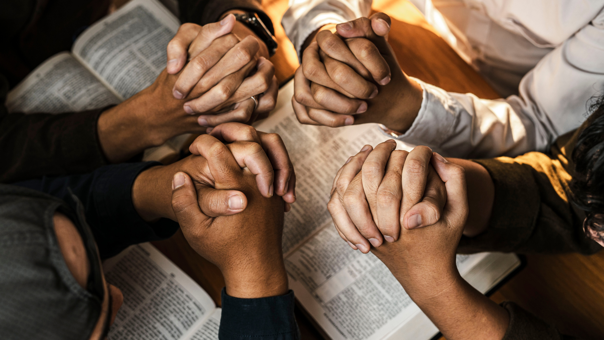 Hands clasped together in a circle over an open book, suggesting prayer or group support.