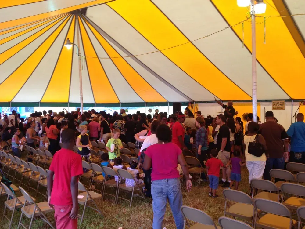 People seated under a yellow-and-white tent at a crowded indoor event