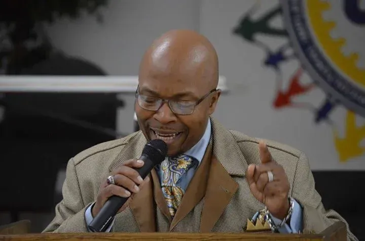 Man speaking at a podium, holding a microphone and raising a finger during a formal event