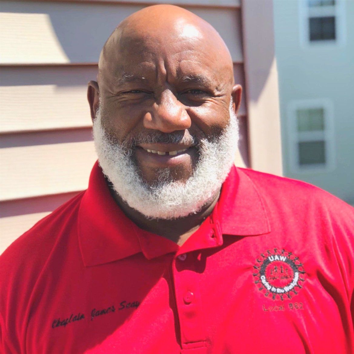 Smiling man in a red polo shirt standing outdoors in sunlight