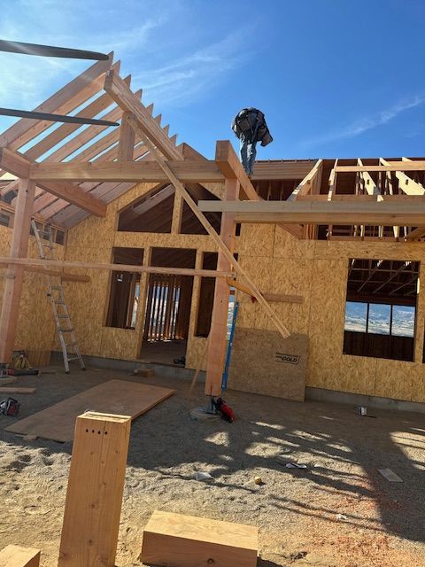 Construction of a wood-framed house; a worker on the roof, building materials, sunny day.