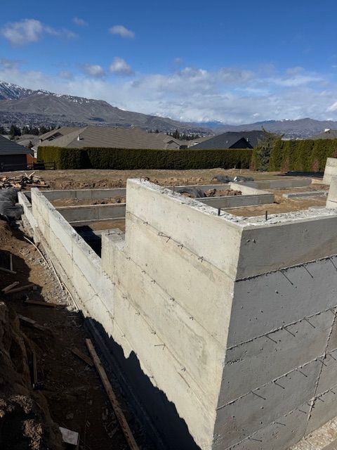 Concrete foundation walls under construction on a sunny day, with mountains in the background.
