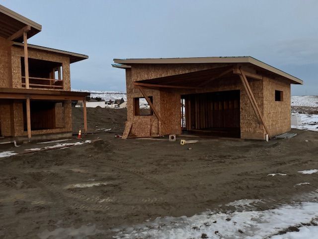 Construction site: unfinished wooden house and garage with open garage door, cloudy sky.
