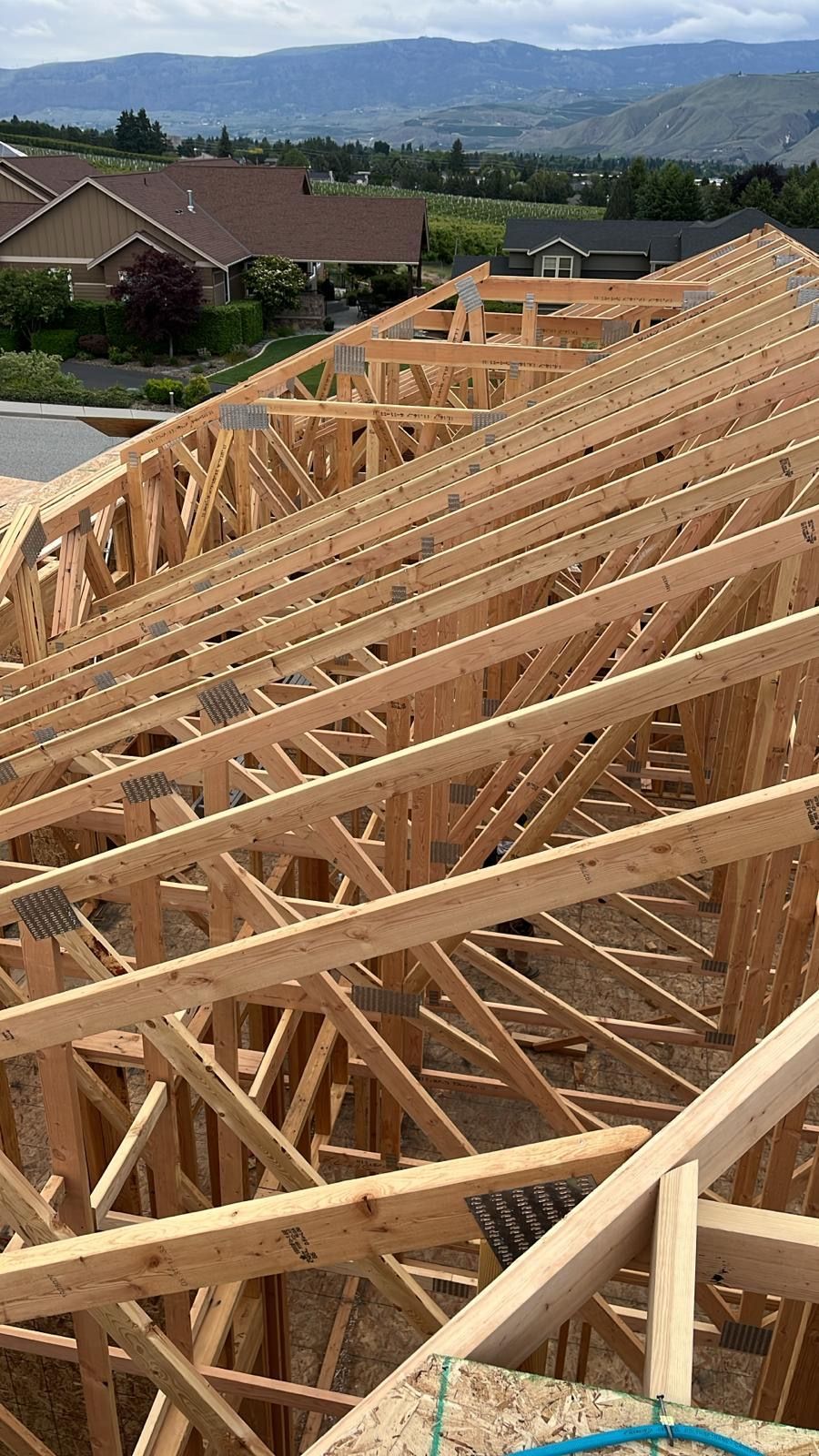 Wooden roof trusses being installed on a house under construction, with a neighborhood and hills in the background.